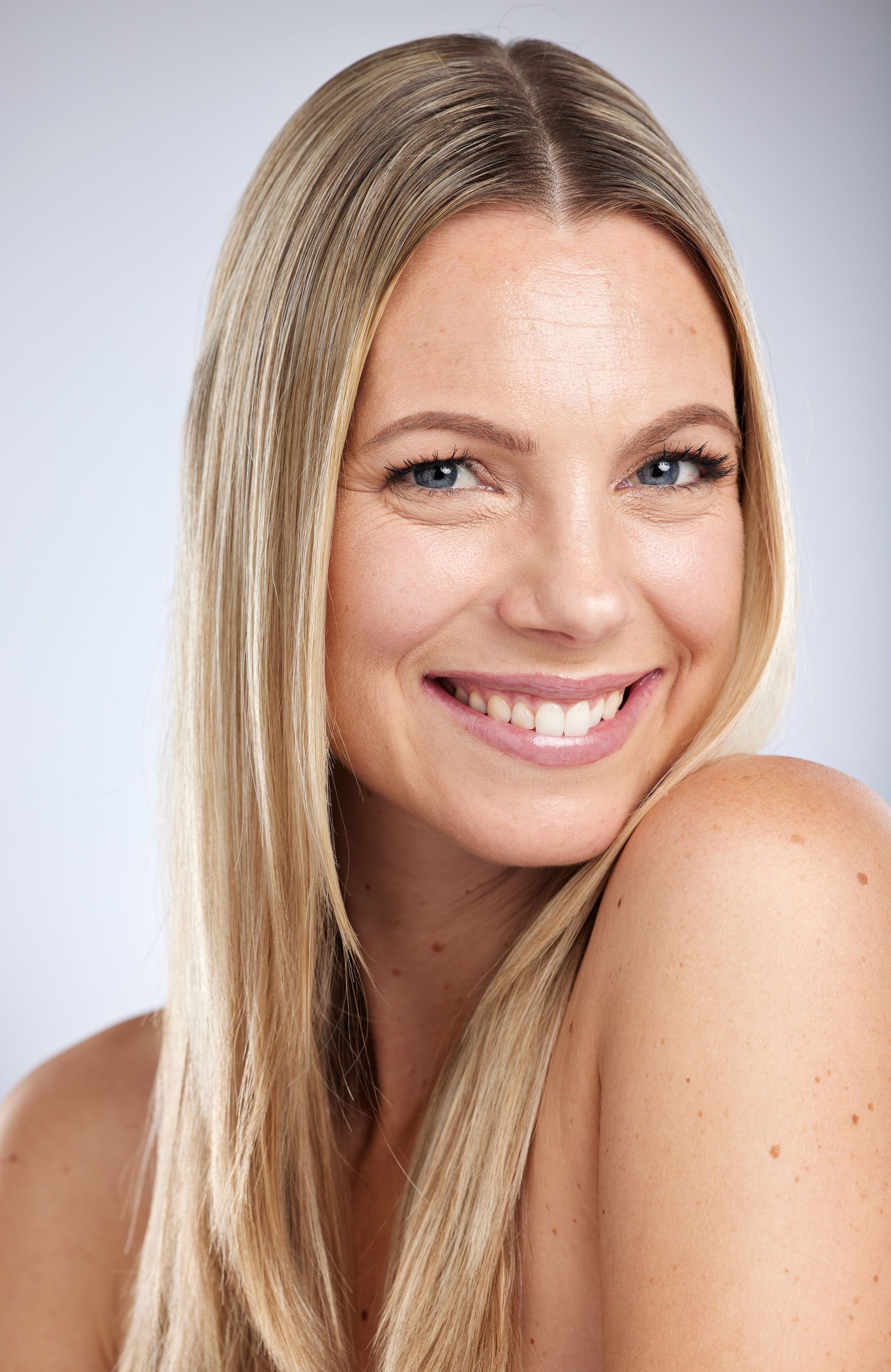 A woman with long blonde hair is smiling and looking at the camera.