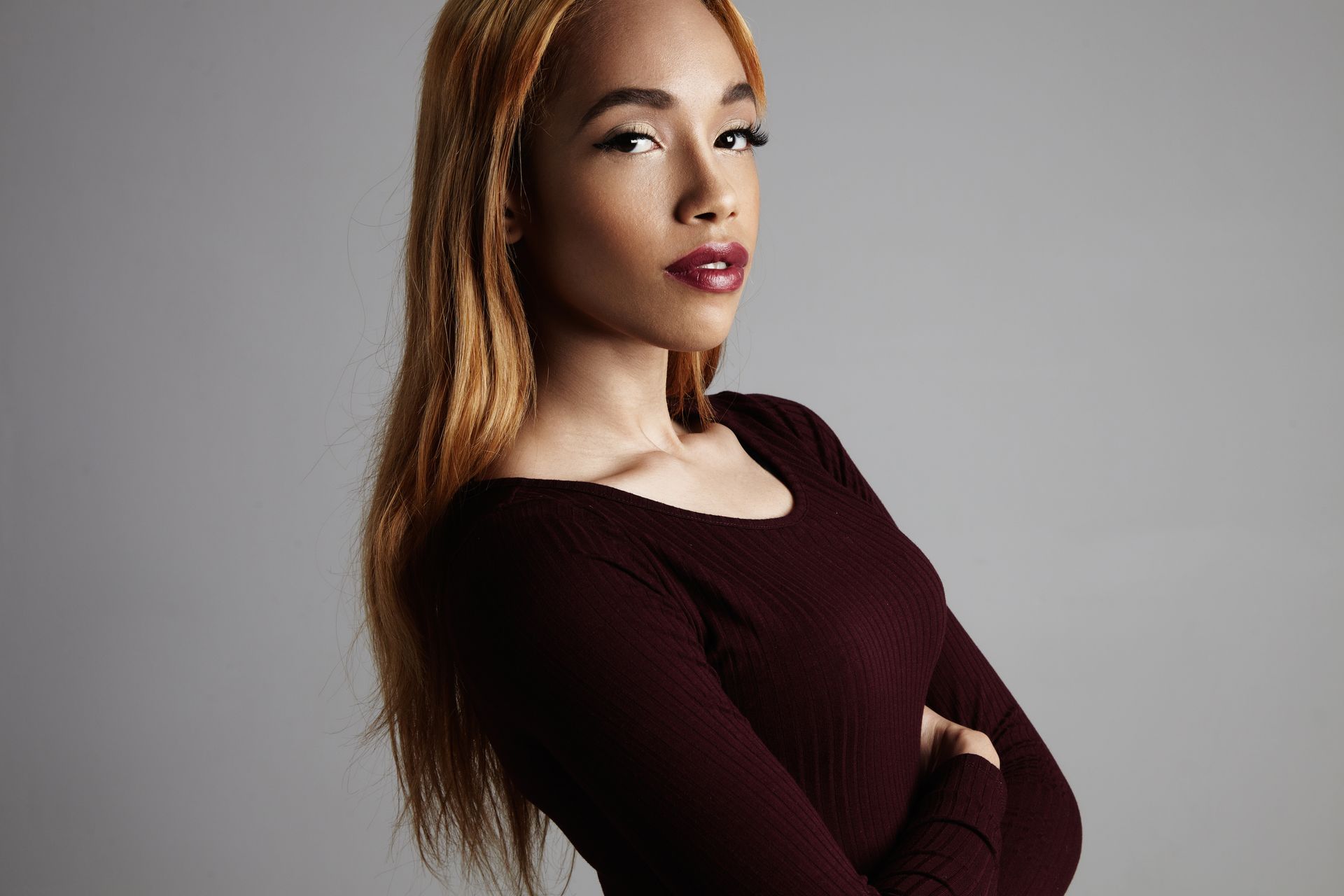 A woman in a maroon sweater is standing with her arms crossed.