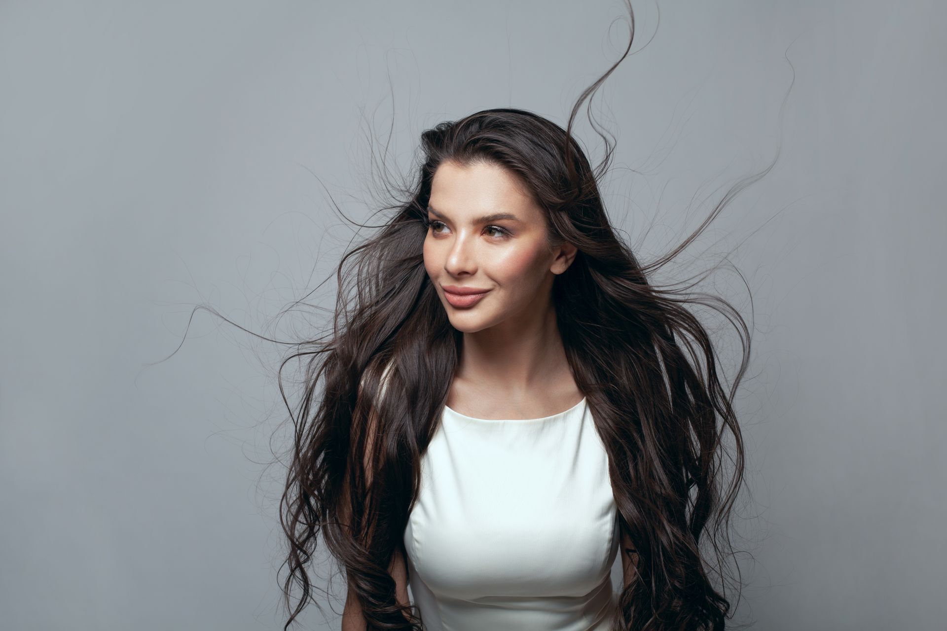 A woman with long hair is wearing a white dress and her hair is blowing in the wind.