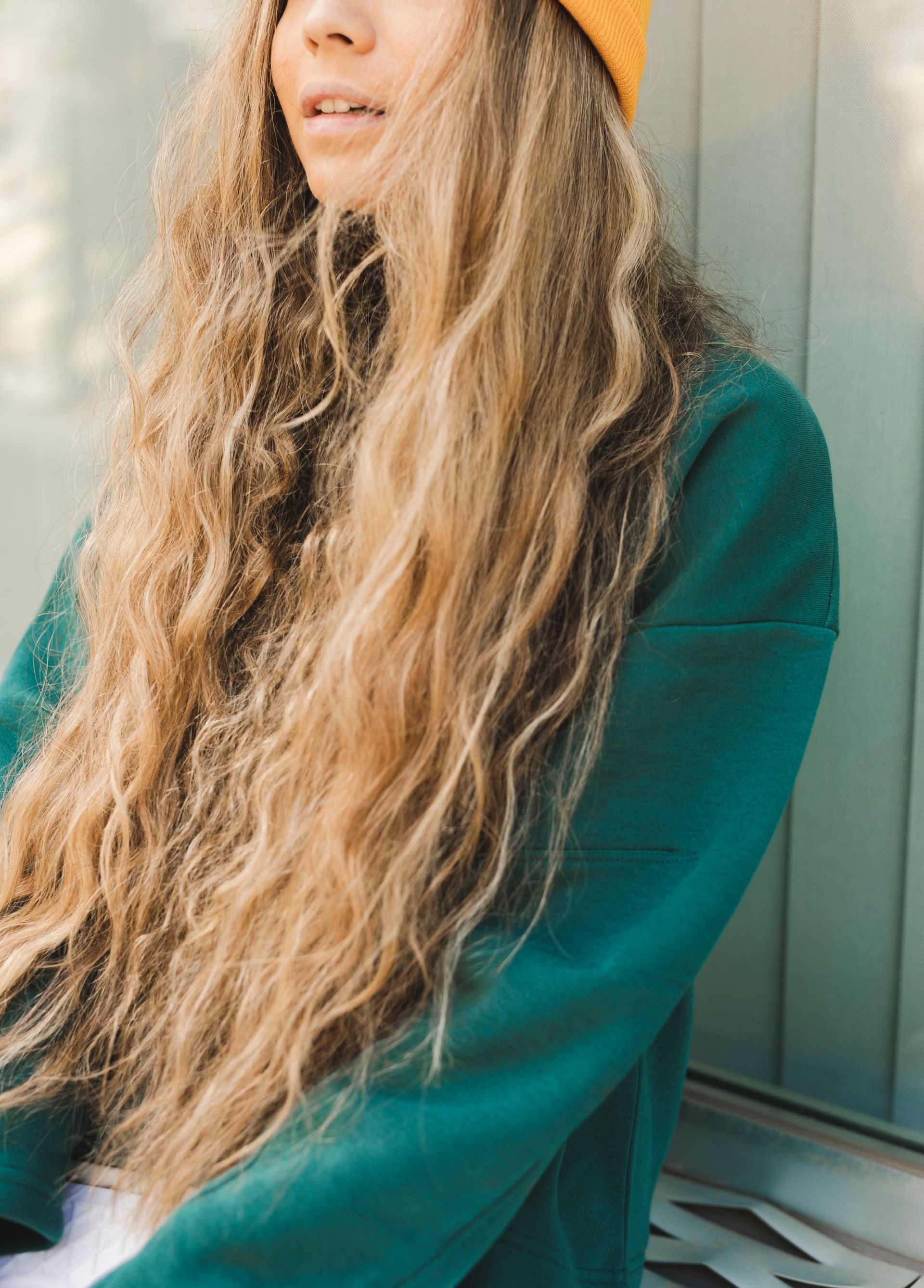 A woman with long blonde hair is wearing a green sweater and a yellow hat.