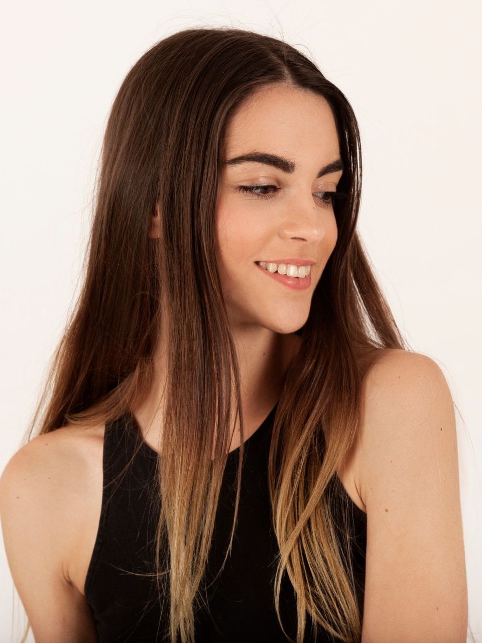 A woman with long hair is wearing a black tank top and smiling.