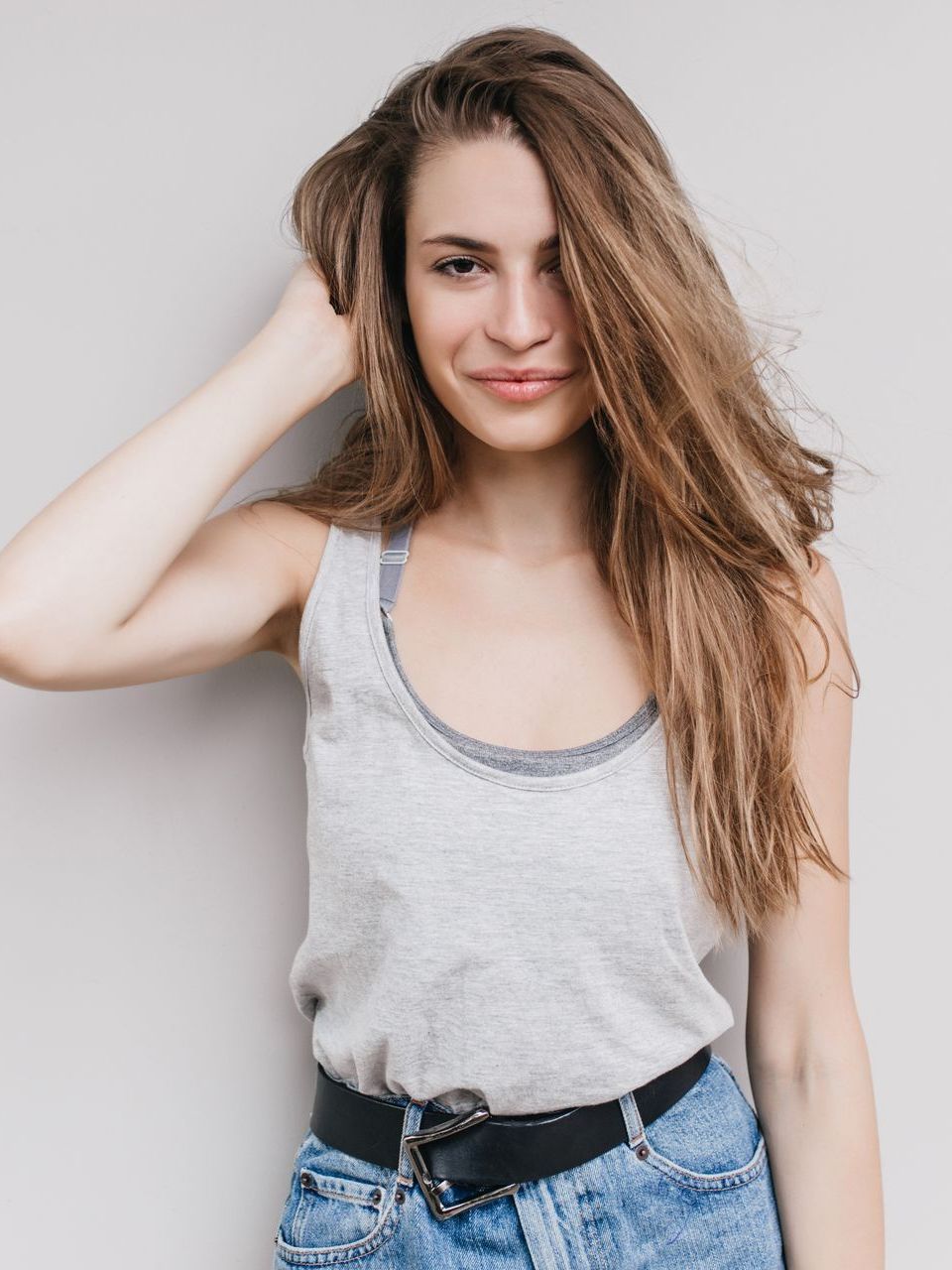 A woman in a tank top and jeans is standing in front of a wall.