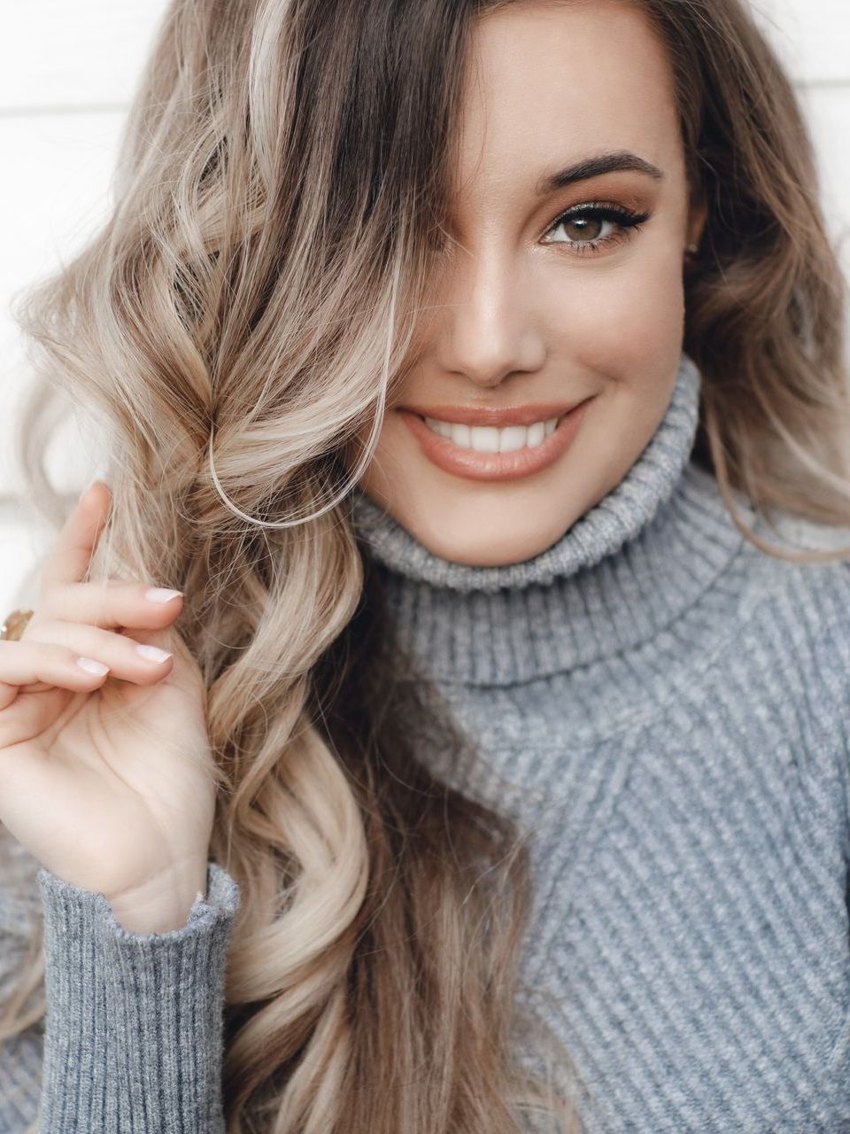 A woman in a turtleneck sweater is smiling and holding her hair.