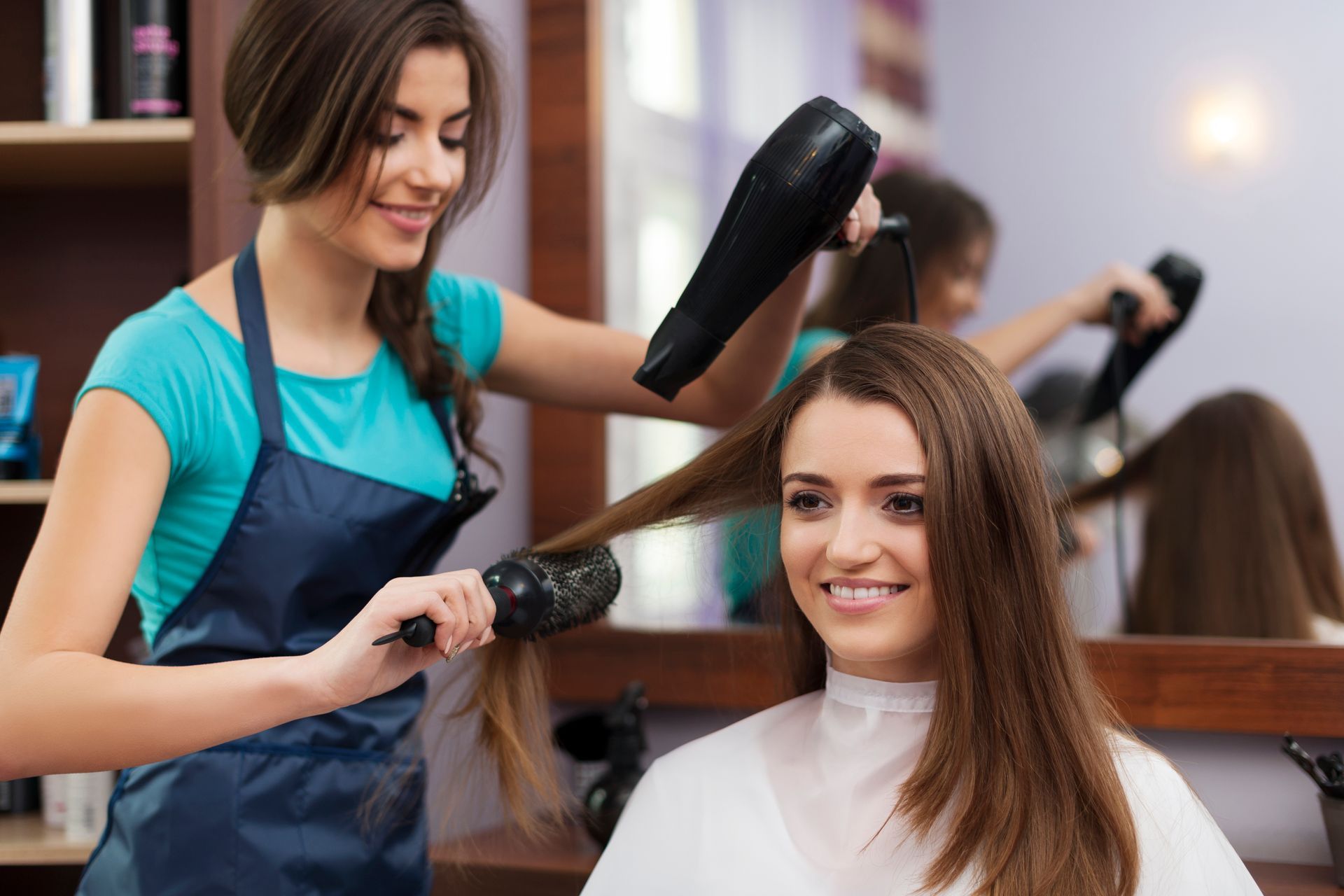 A woman is getting her hair blow dried by a hairdresser in a salon.