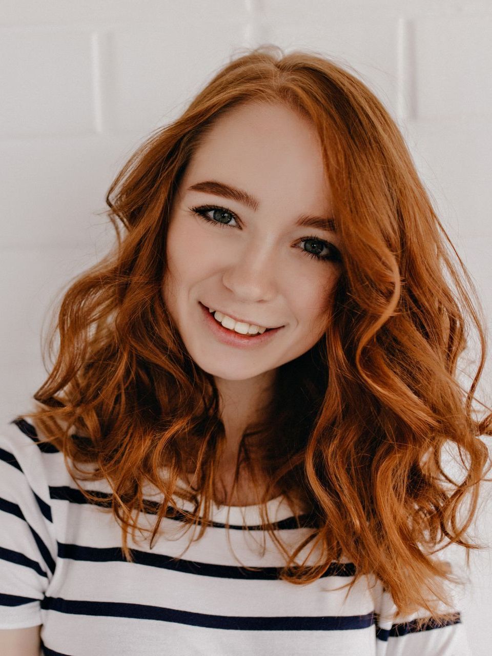 A woman with red hair is wearing a striped shirt and smiling.