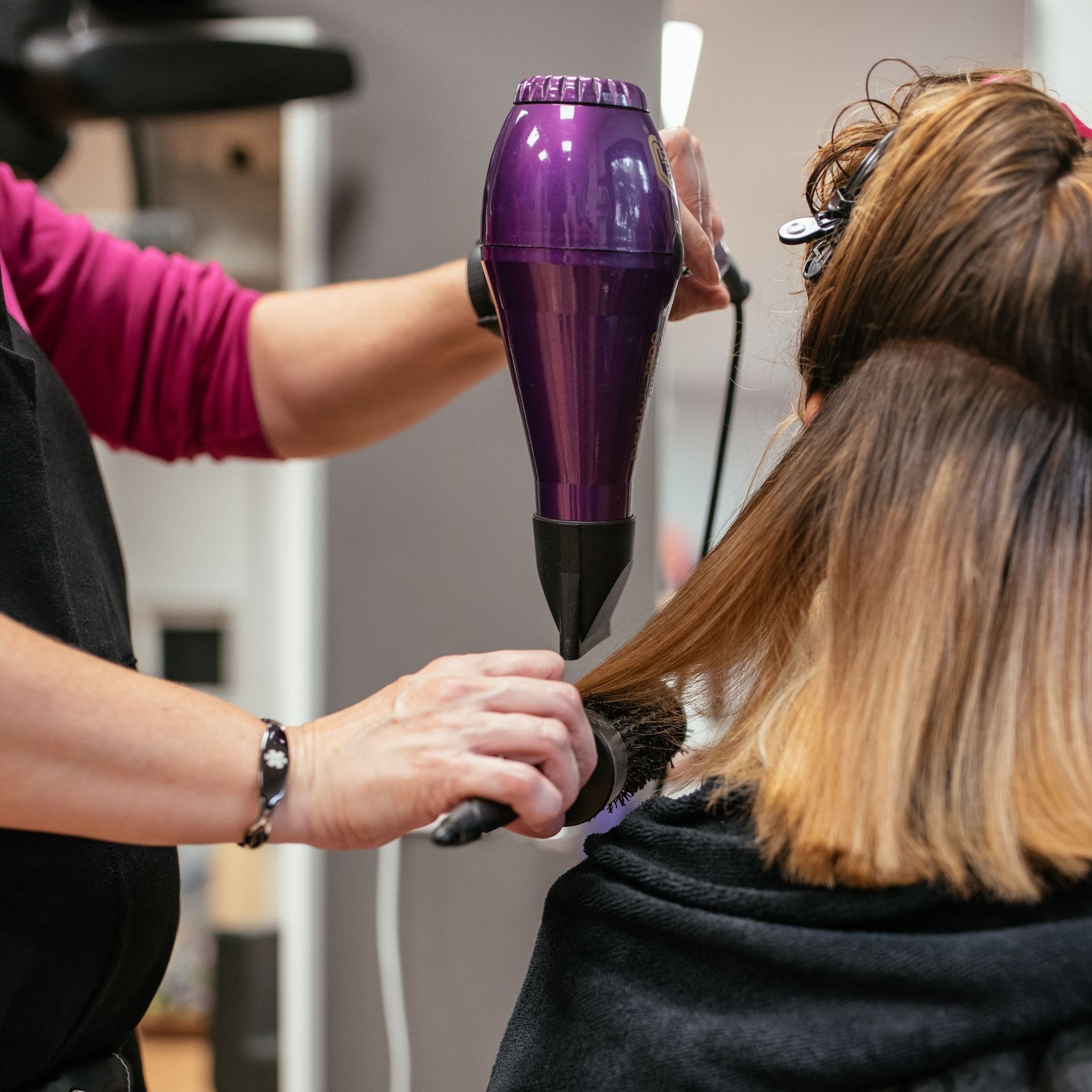 A woman is getting her hair blow dried by a purple hair dryer