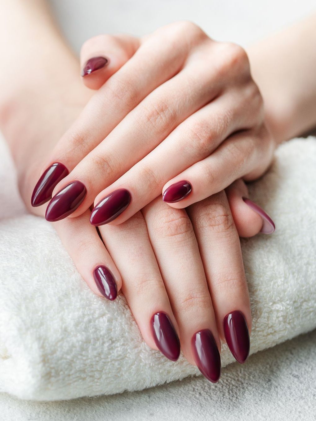 A woman 's hands with burgundy nails are sitting on a white towel.