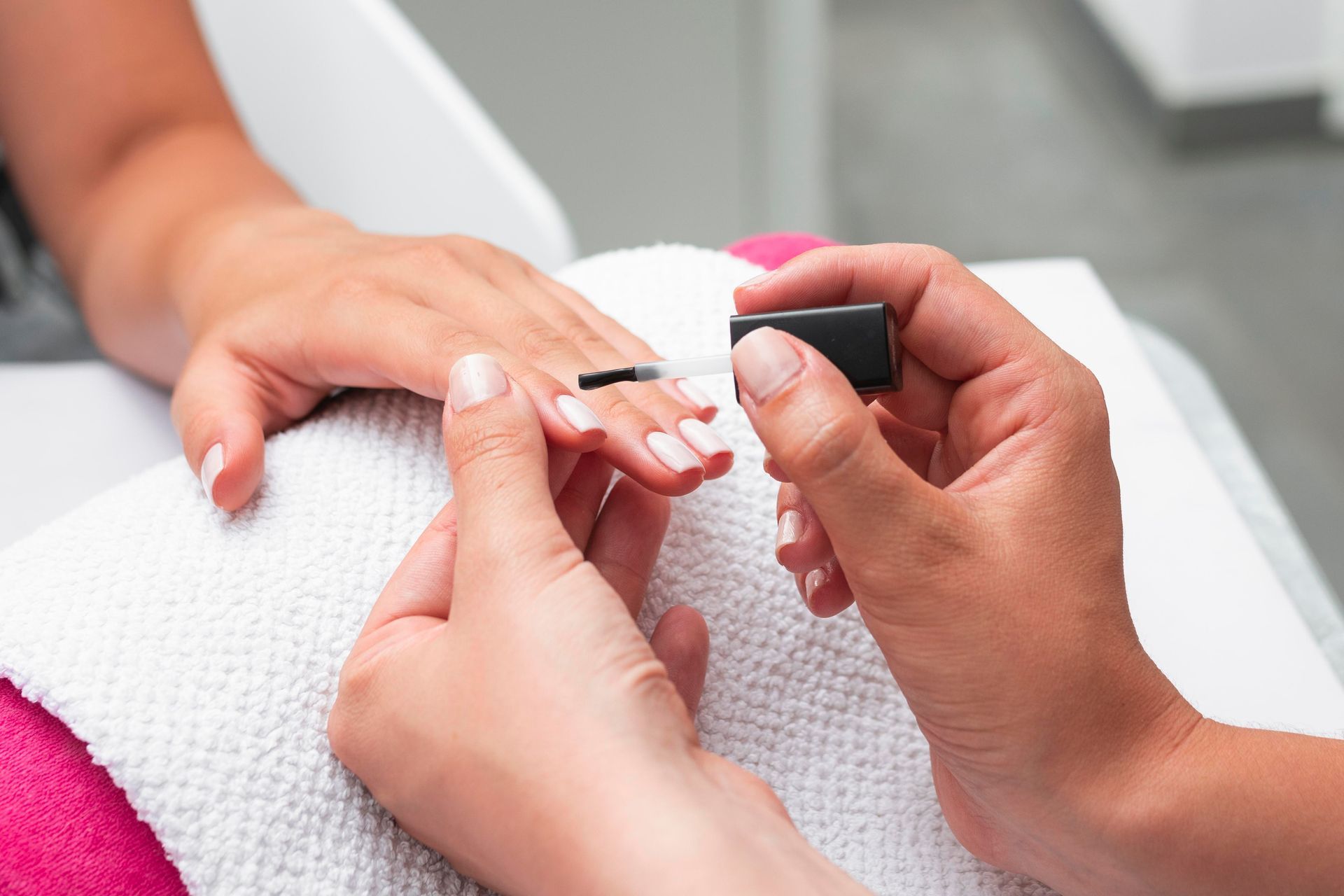 A woman 's hands are on a towel next to a bottle of nail polish.