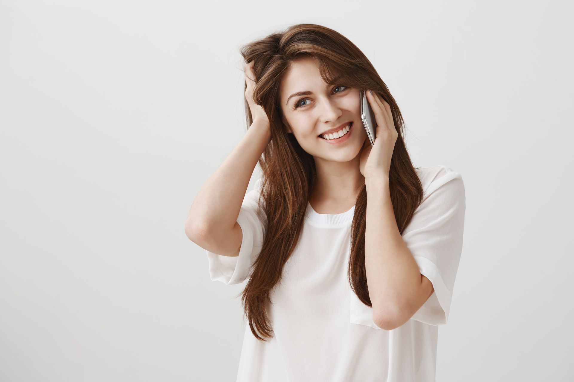 A woman is smiling while talking on a cell phone.