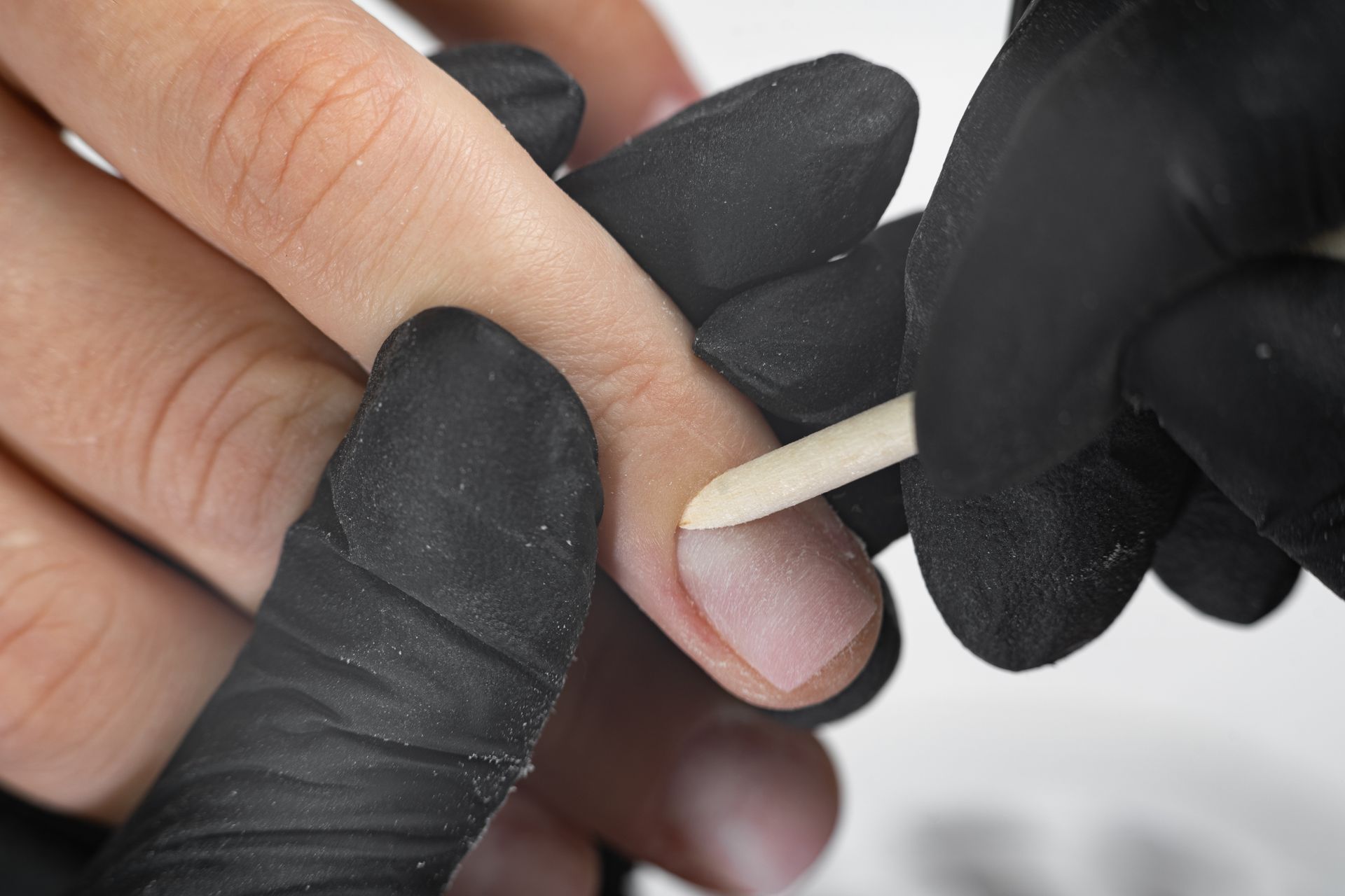 A person wearing black gloves is cutting their nails with a wooden stick.