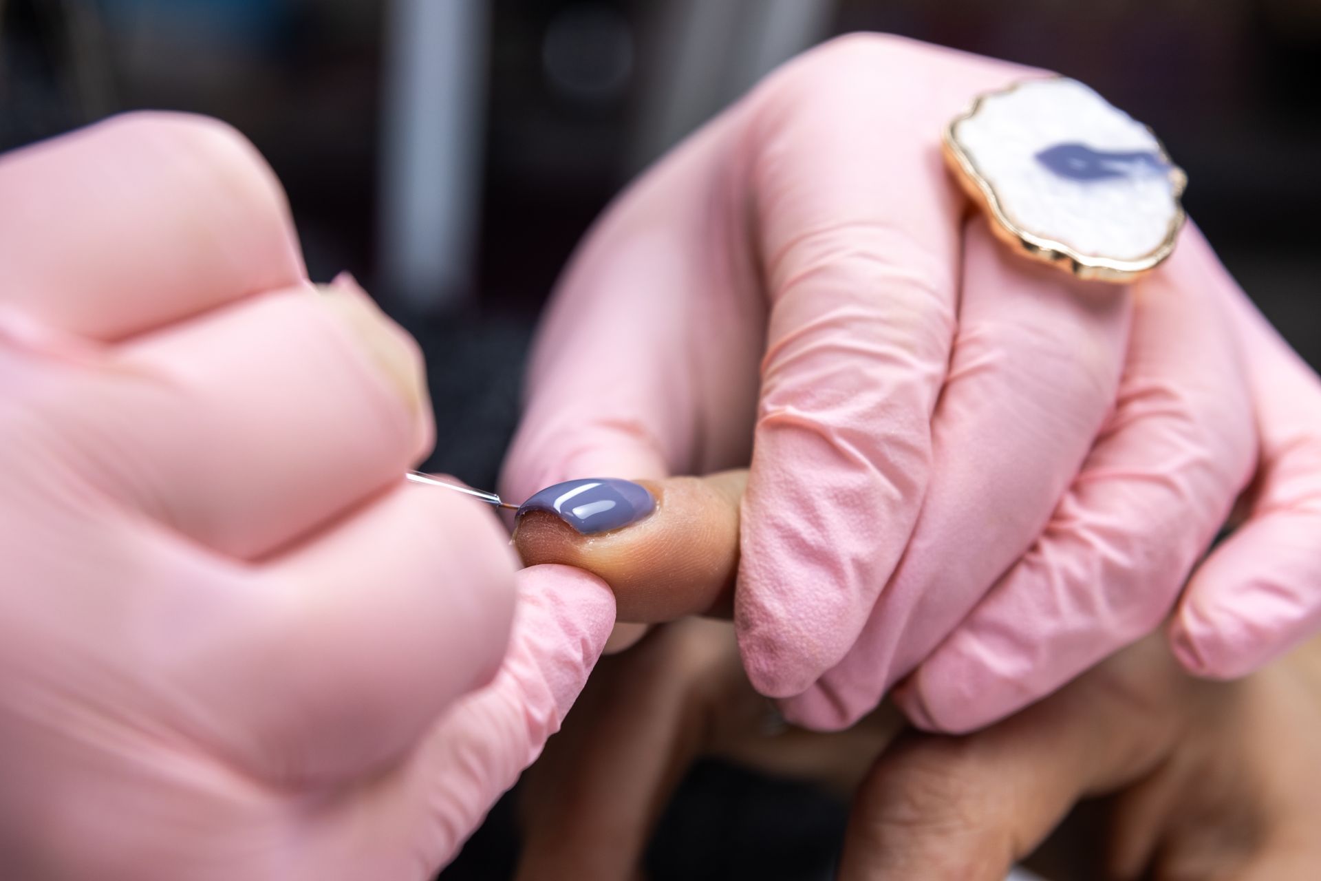 A woman is getting her nails done by a nail artist wearing pink gloves.