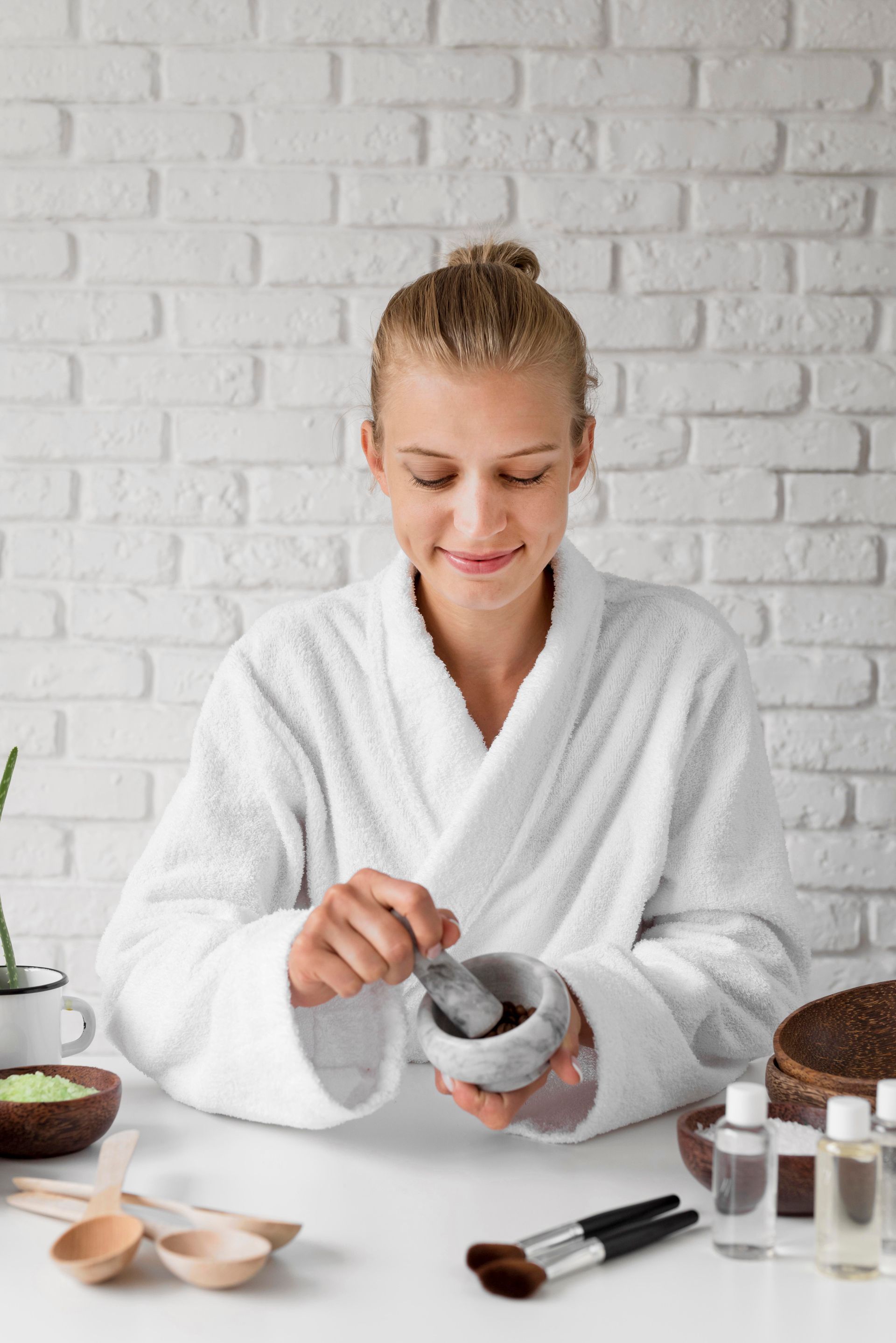 A woman in a bathrobe is making a face mask with a mortar and pestle.