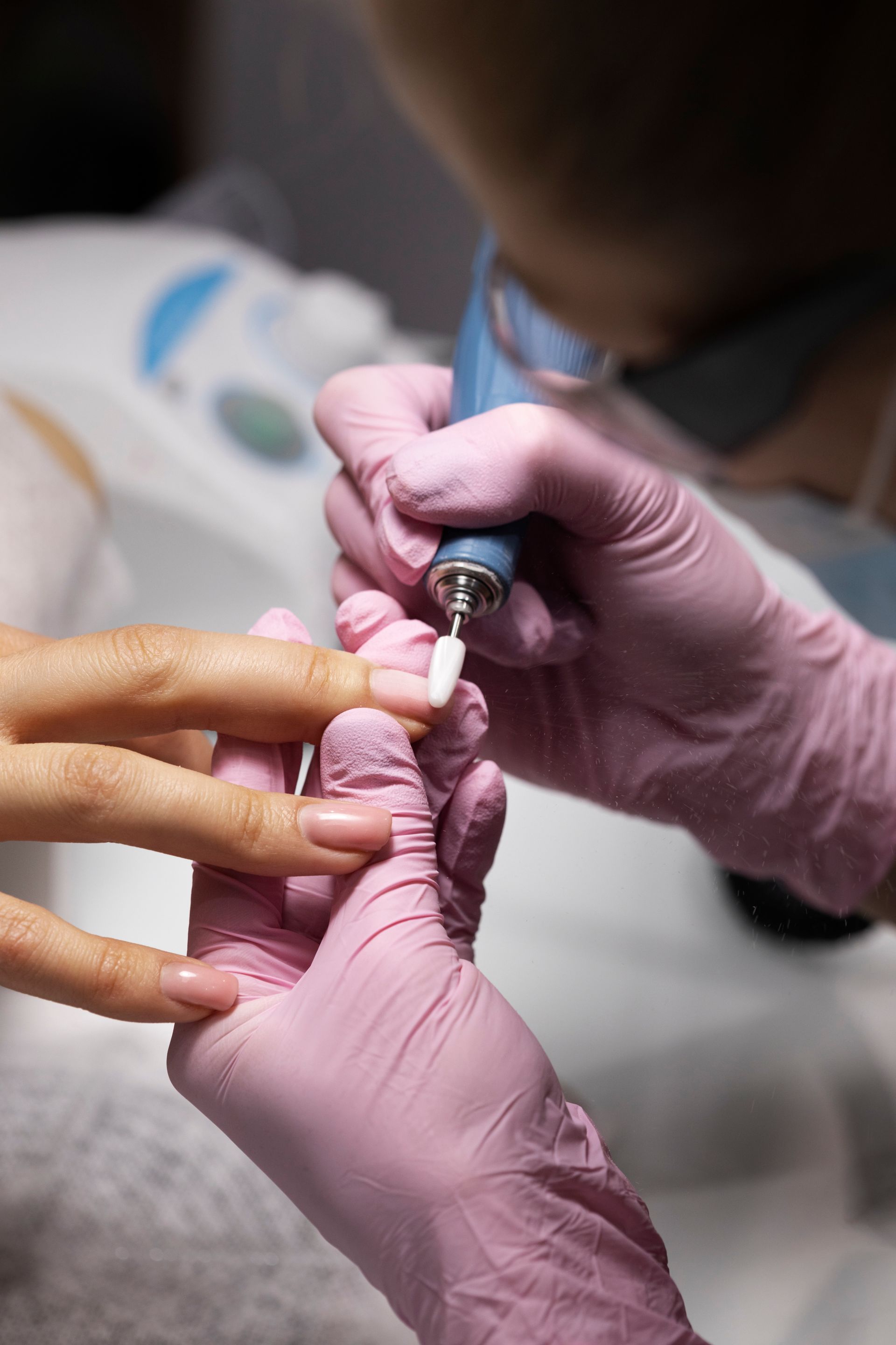 A woman is getting her nails done by a nail artist wearing pink gloves.