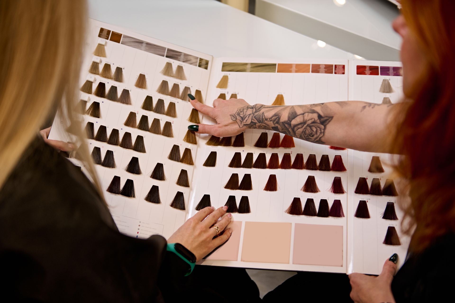 Two women are looking at a book of hair color samples.