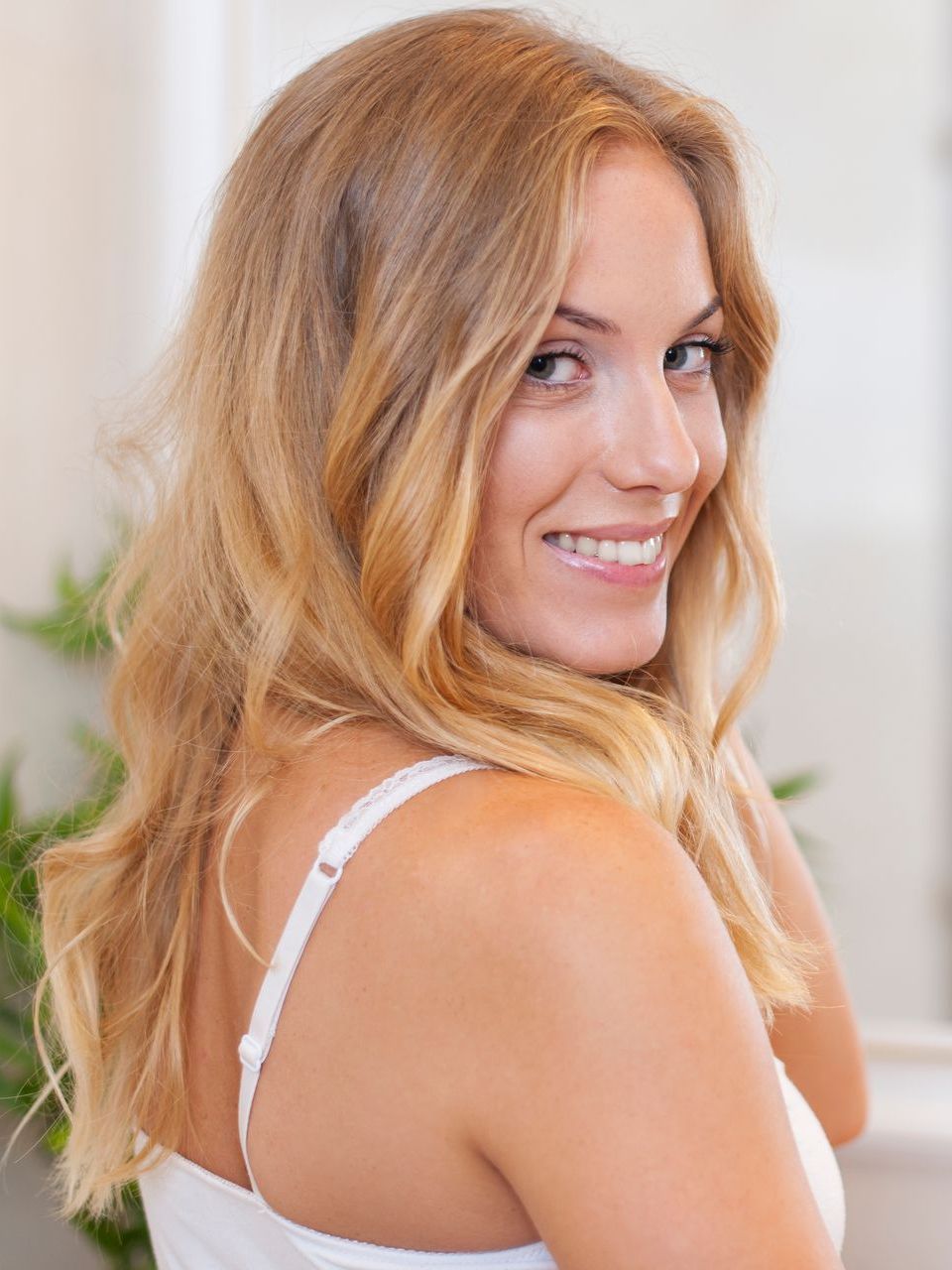 A woman in a white bra is smiling and looking over her shoulder.