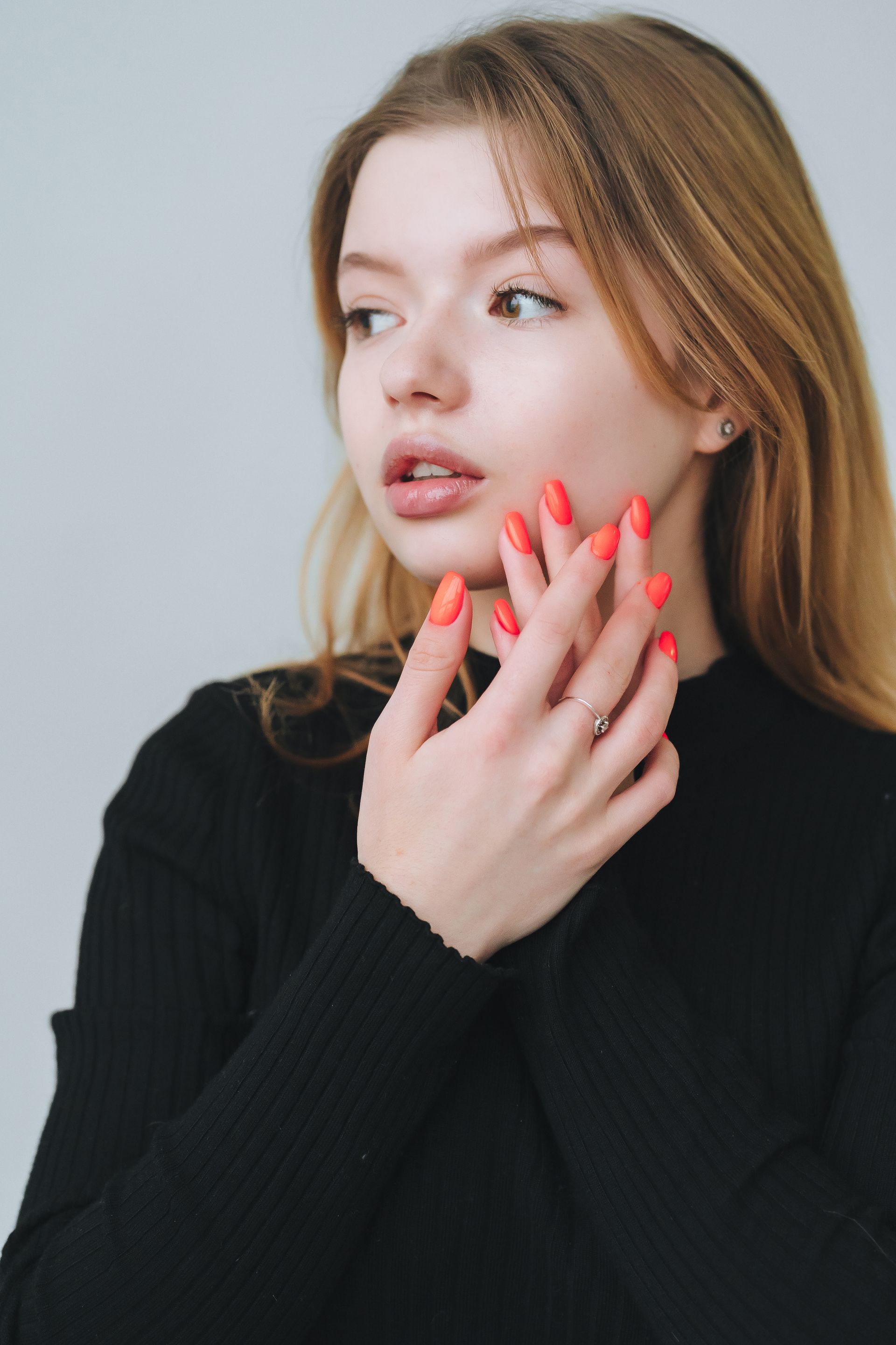 The woman is wearing a black sweater and has red nails.