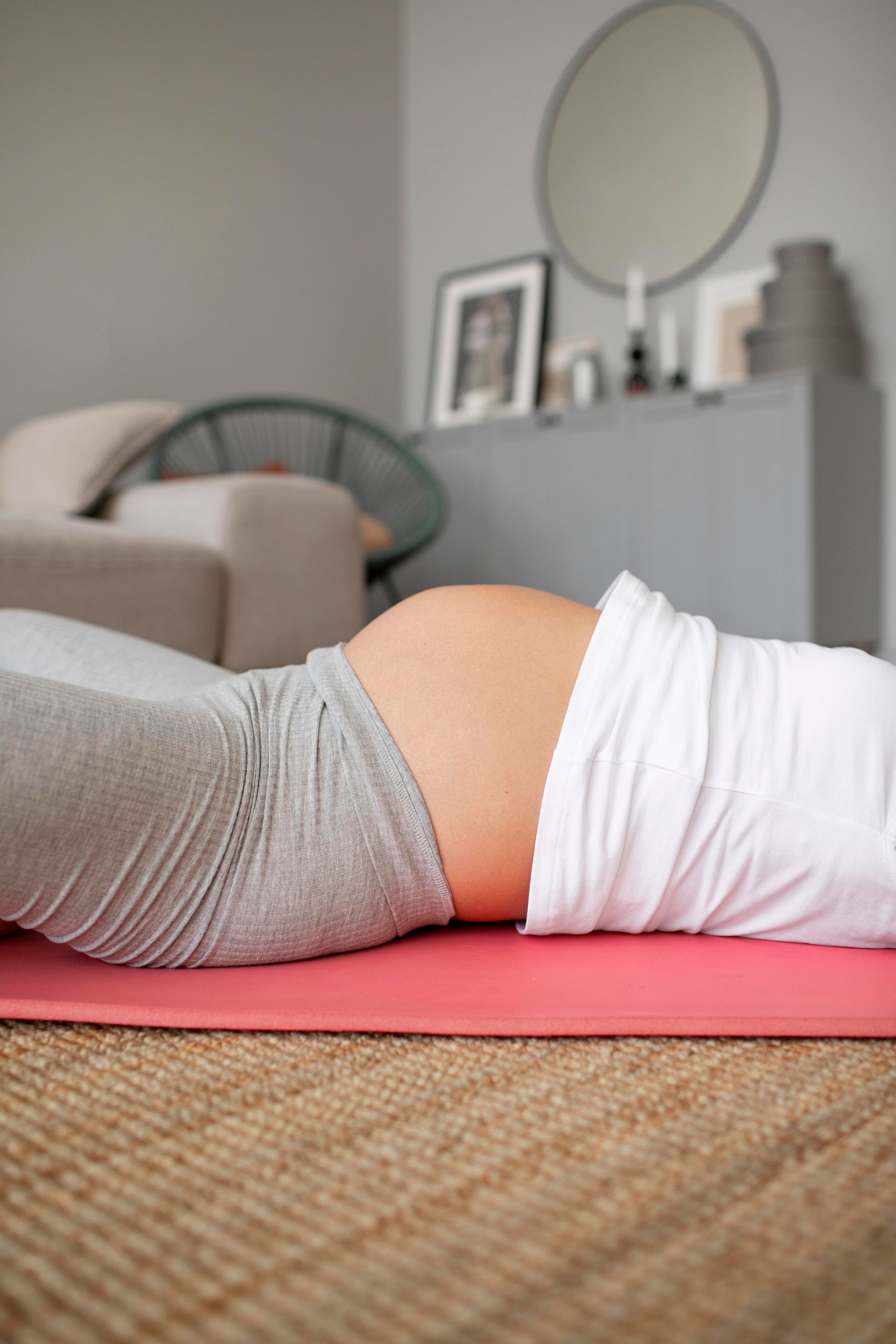 A pregnant woman is laying on a yoga mat in a living room.