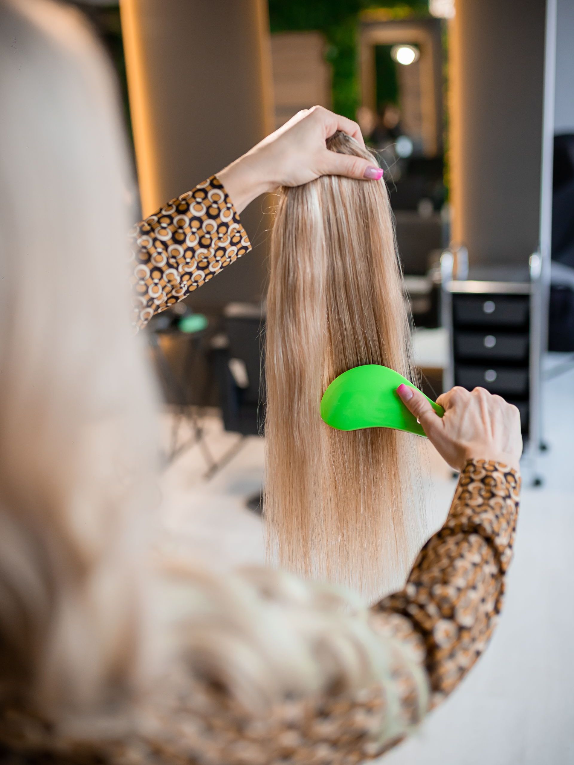 A woman is brushing her hair with a green comb in a salon.