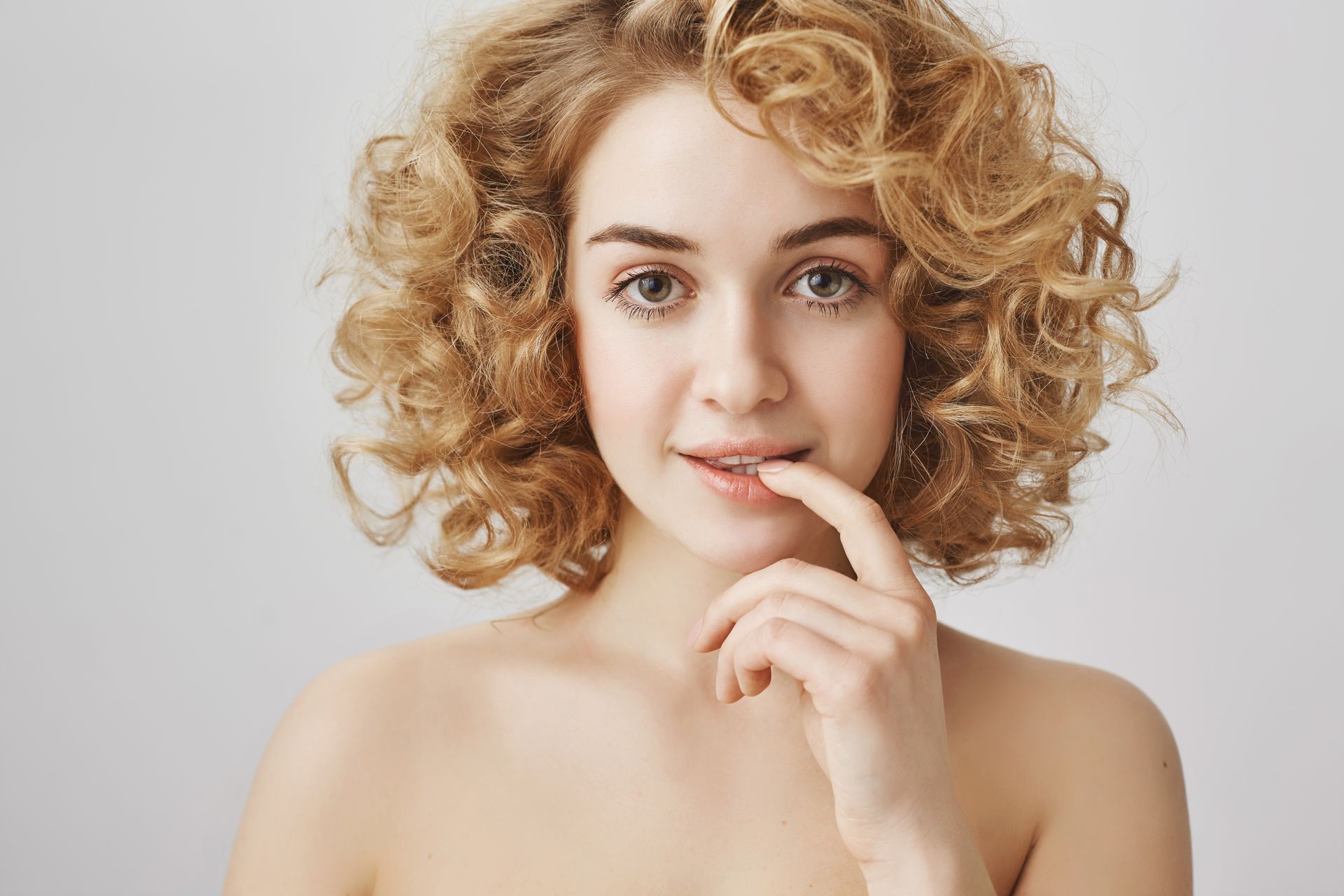 A woman with curly hair is covering her mouth with her finger.