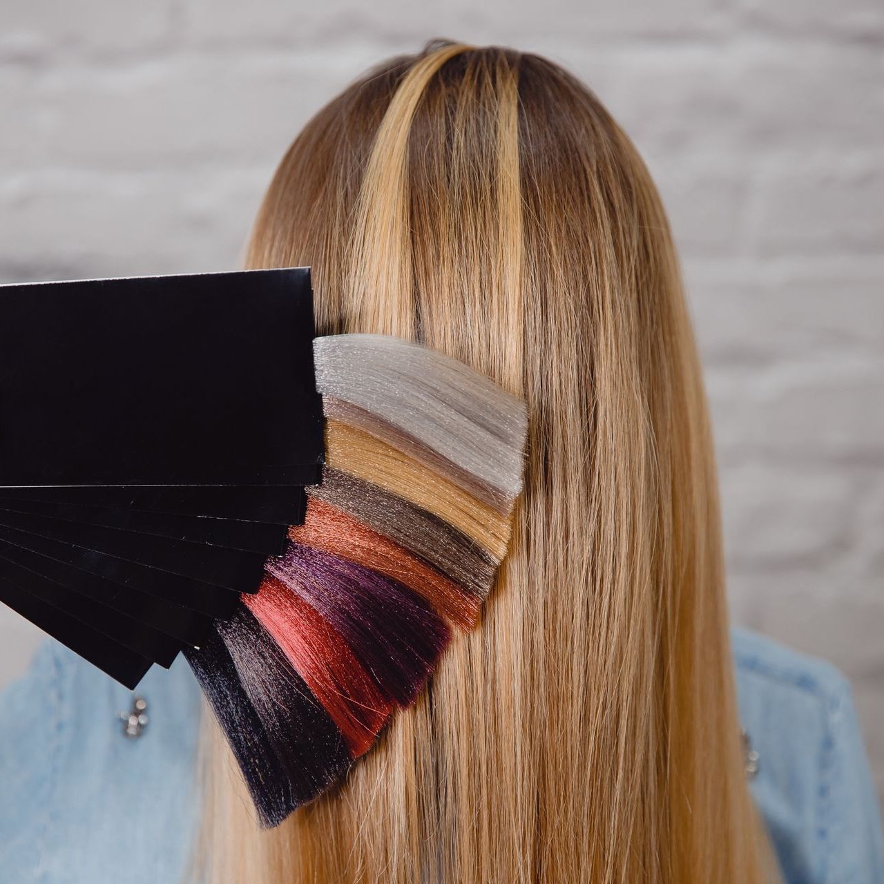 A woman is holding a palette of hair colors in front of her hair.