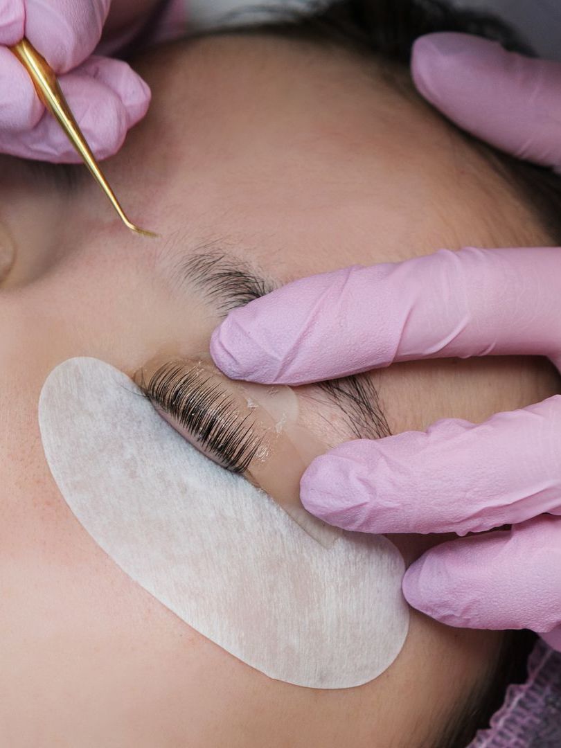 A woman wearing pink gloves is getting eyelash extensions.