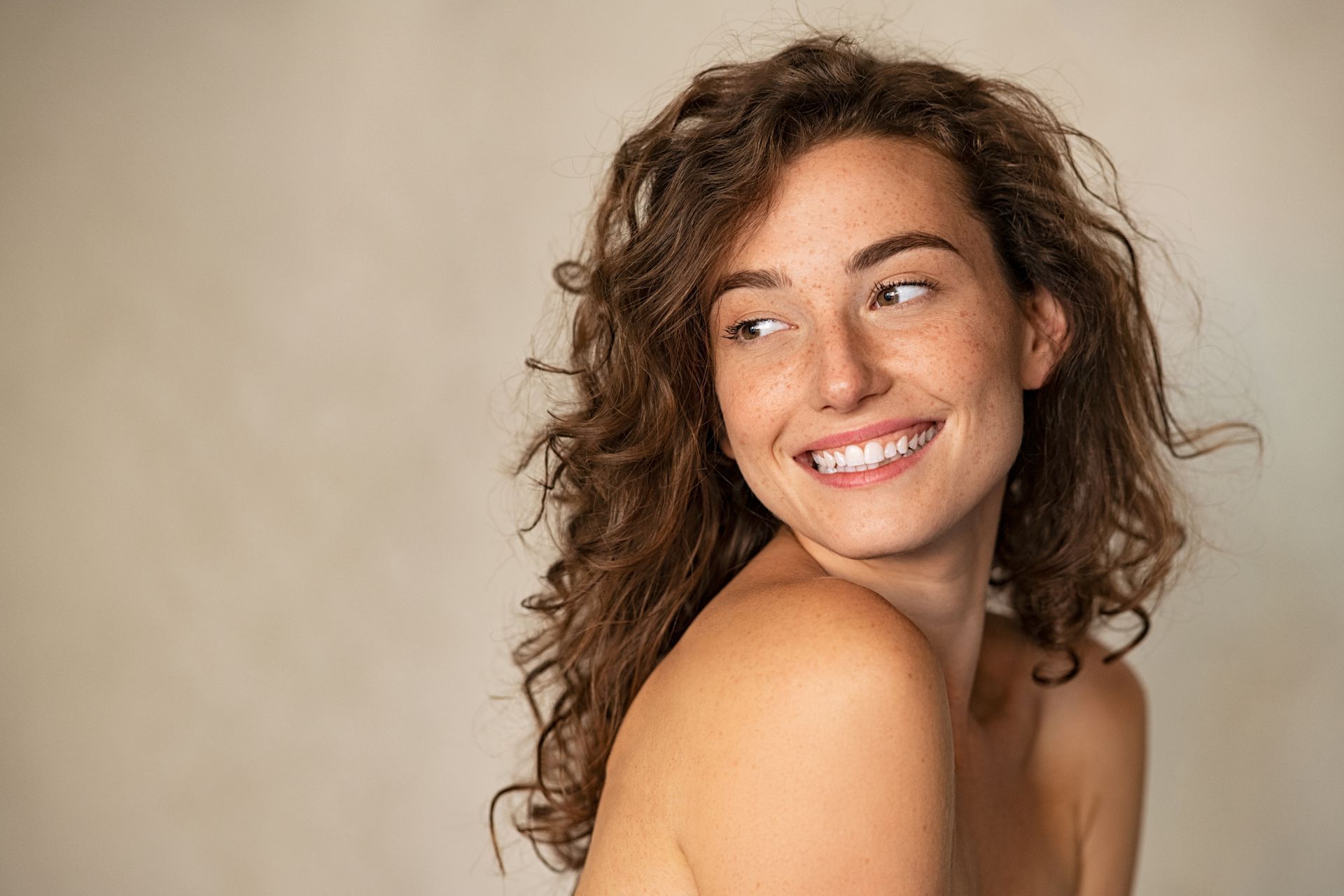 A woman with curly hair is smiling and looking over her shoulder.