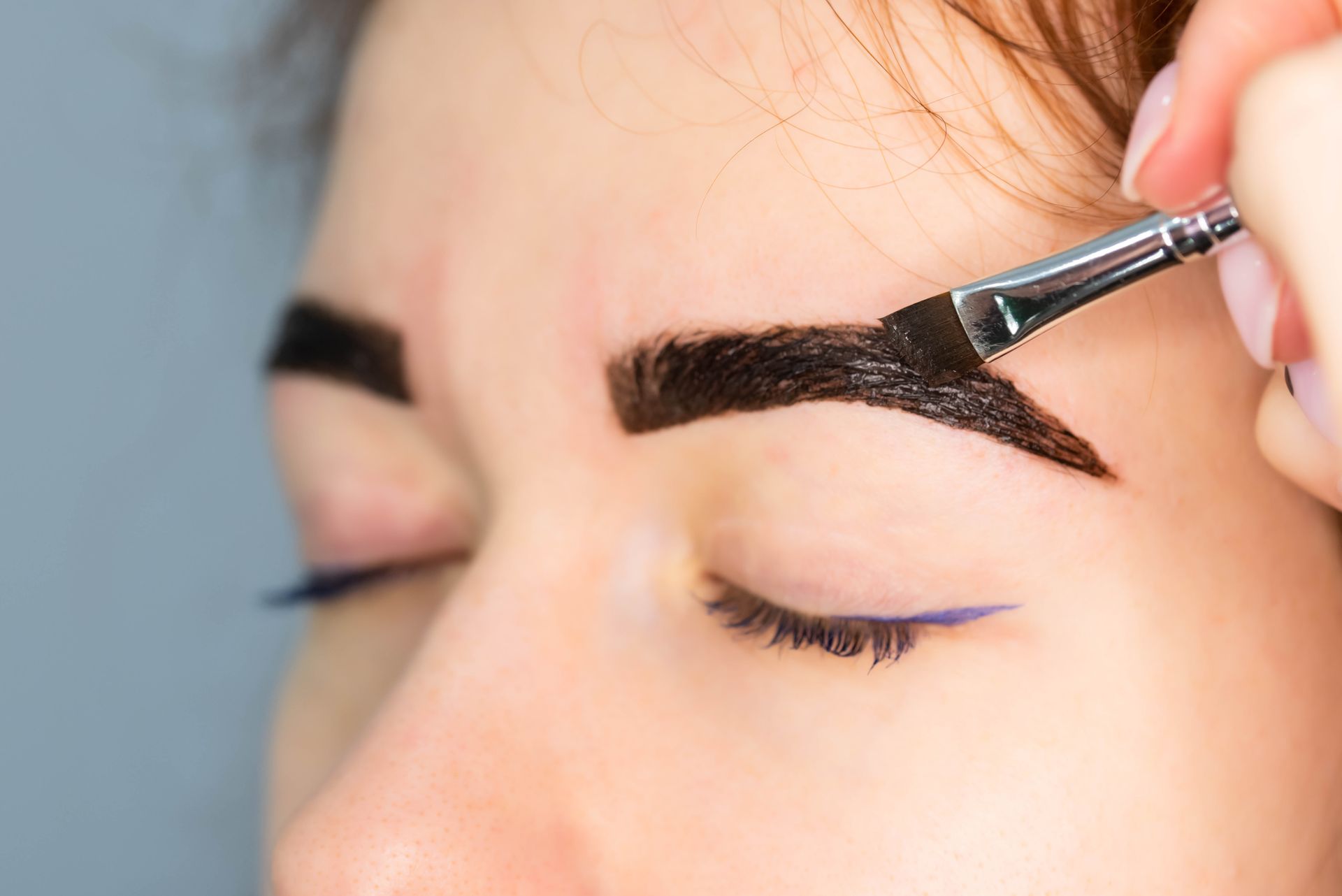 A woman is applying henna to her eyebrows with a brush.