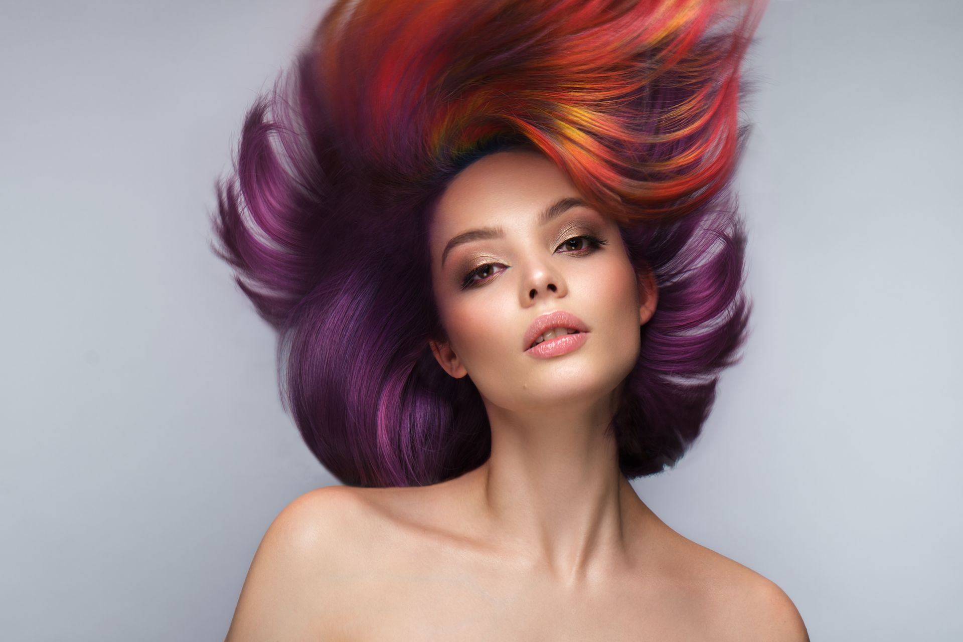 A woman with colorful hair is laying down with her hair blowing in the wind.