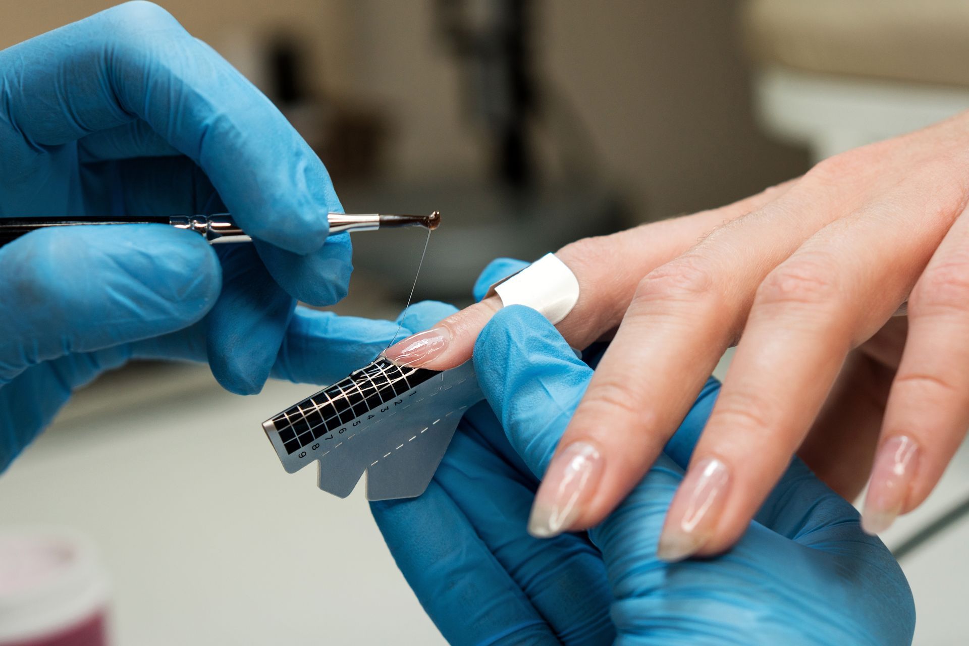 A woman is getting her nails done by a nail artist wearing blue gloves.