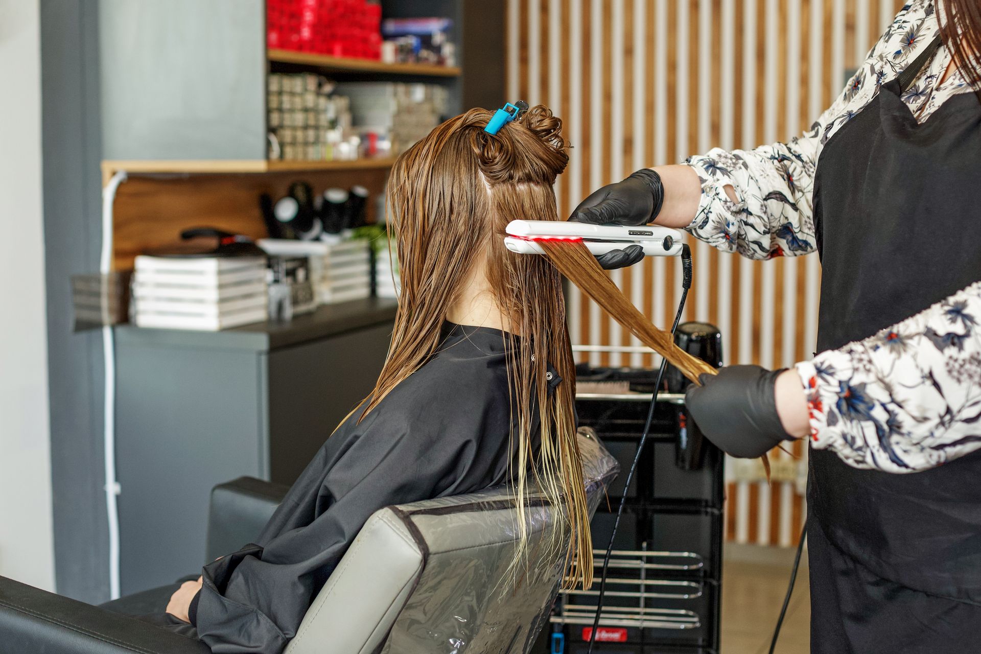 A woman is getting her hair straightened by a hairdresser in a salon.