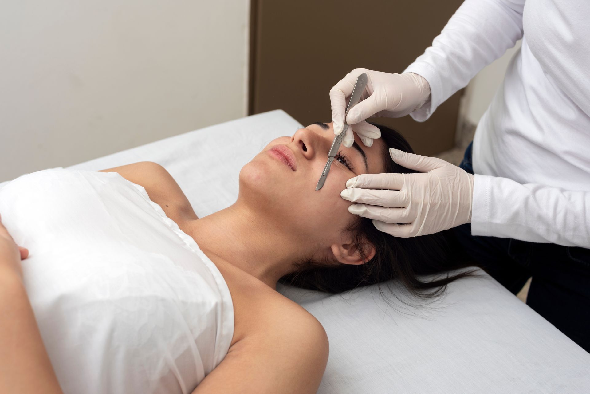 A woman is laying on a bed getting her eyebrows measured by a doctor.