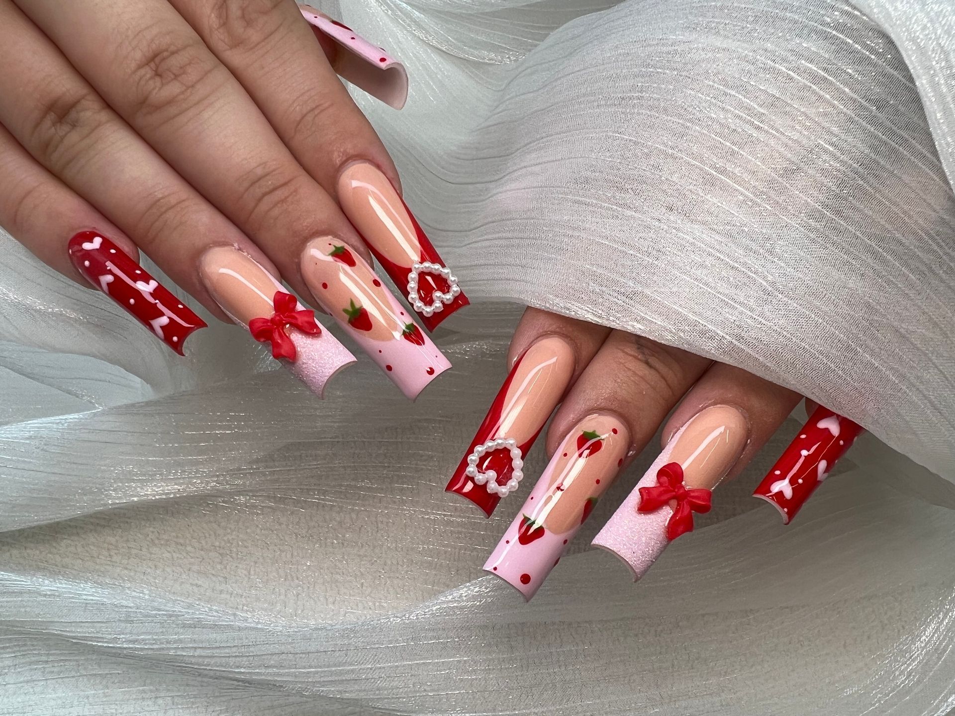 A close up of a person 's nails with strawberries and bows on them.