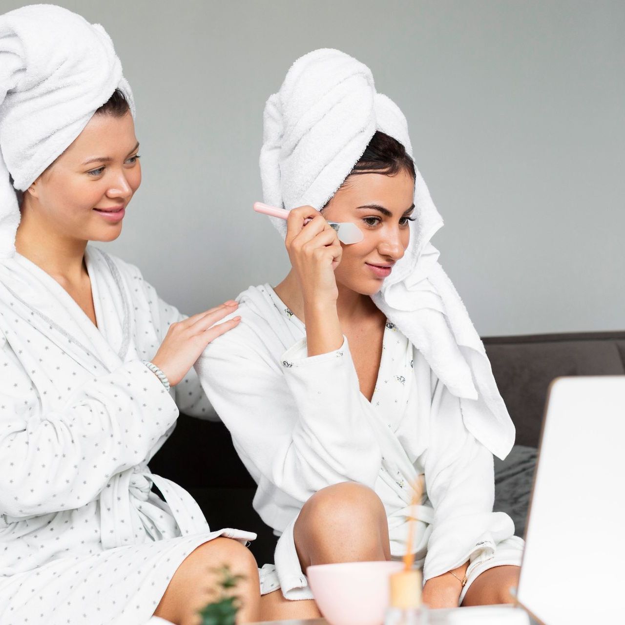 Two women with towels wrapped around their heads are looking at a laptop.