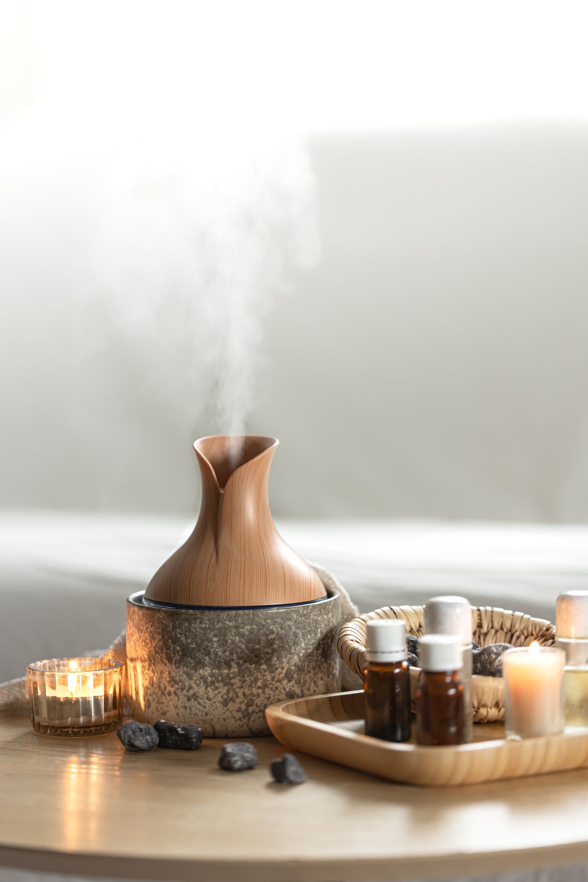 A wooden essential oil diffuser is sitting on a wooden table next to candles and rocks.