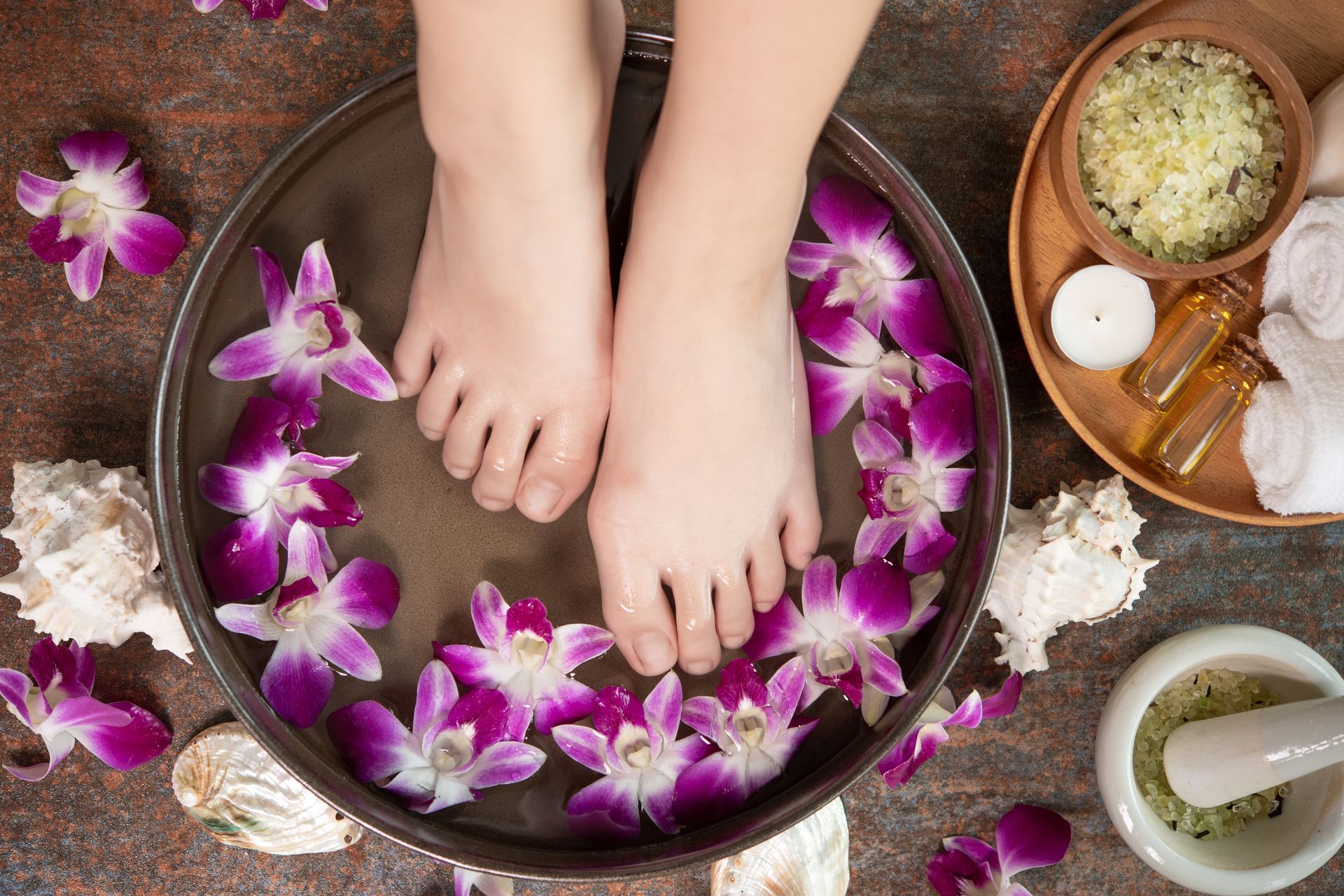 A woman 's feet are in a bowl of water with purple flowers.