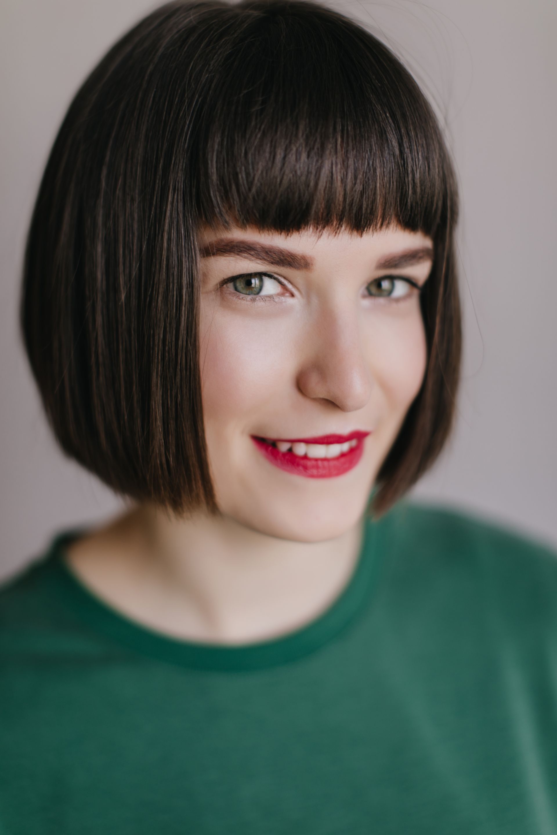 A woman with short hair and bangs is wearing a green shirt and red lipstick.