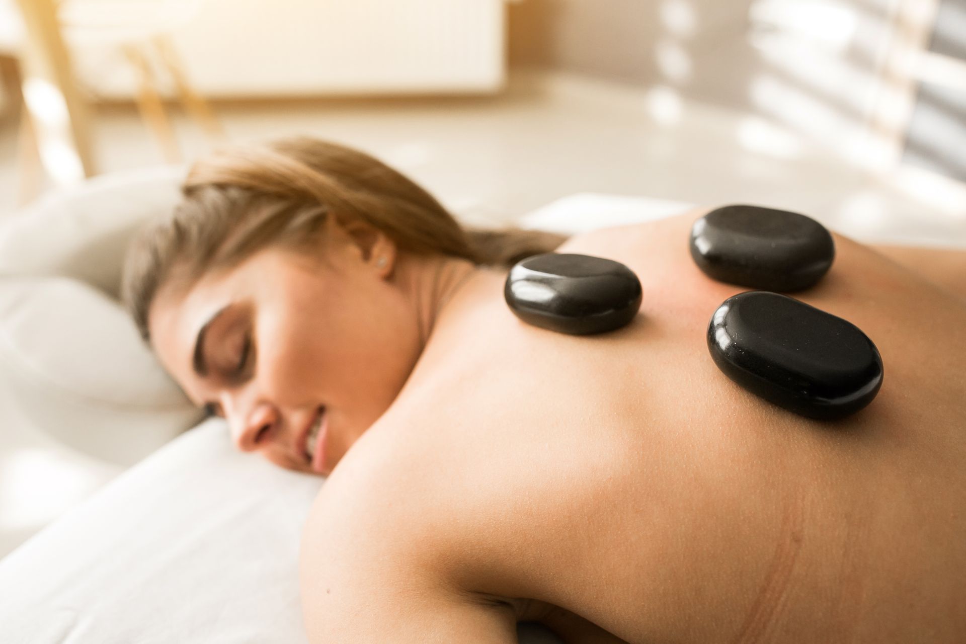 A woman is laying on a bed getting a hot stone massage.