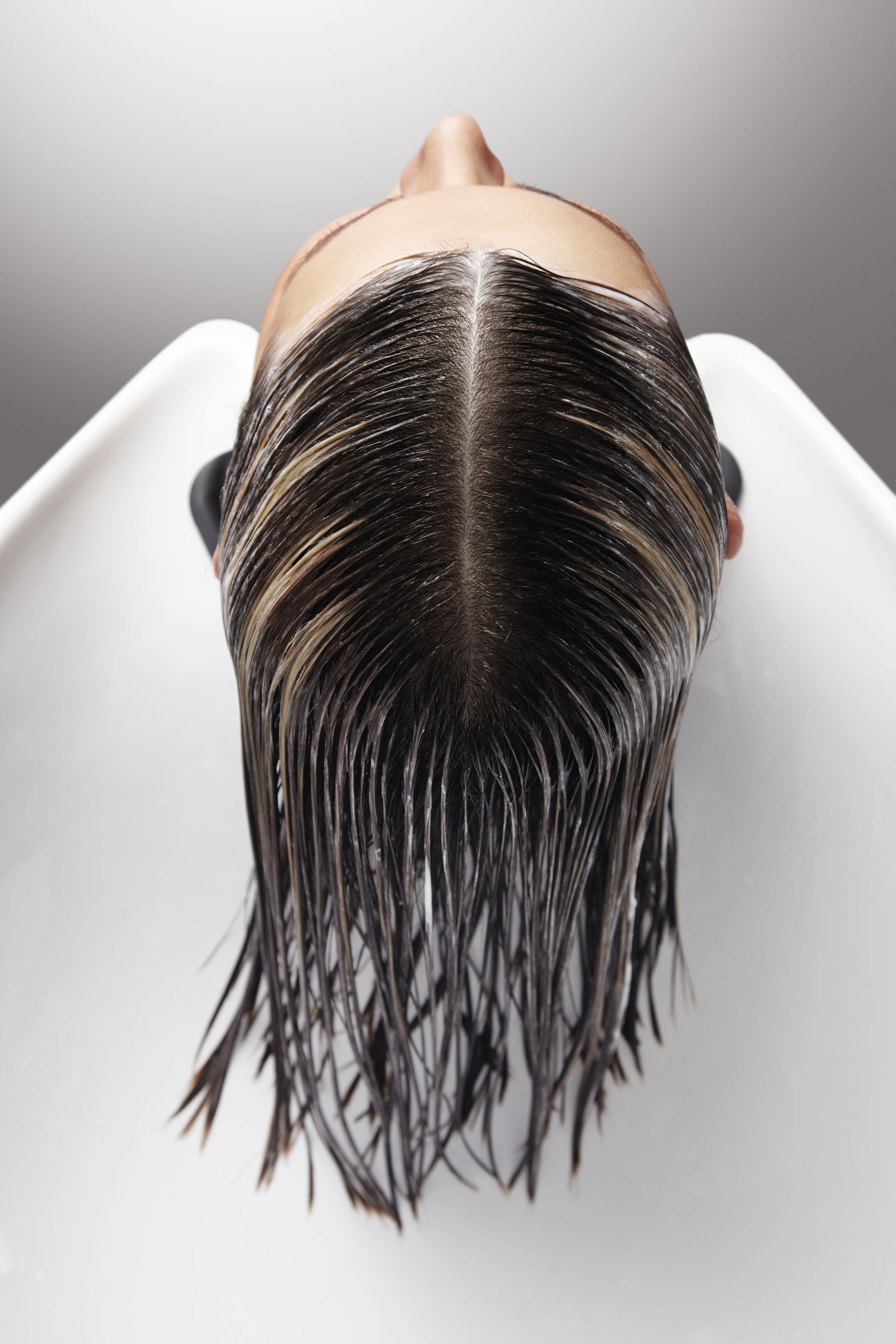 A woman is washing her hair in a white sink.