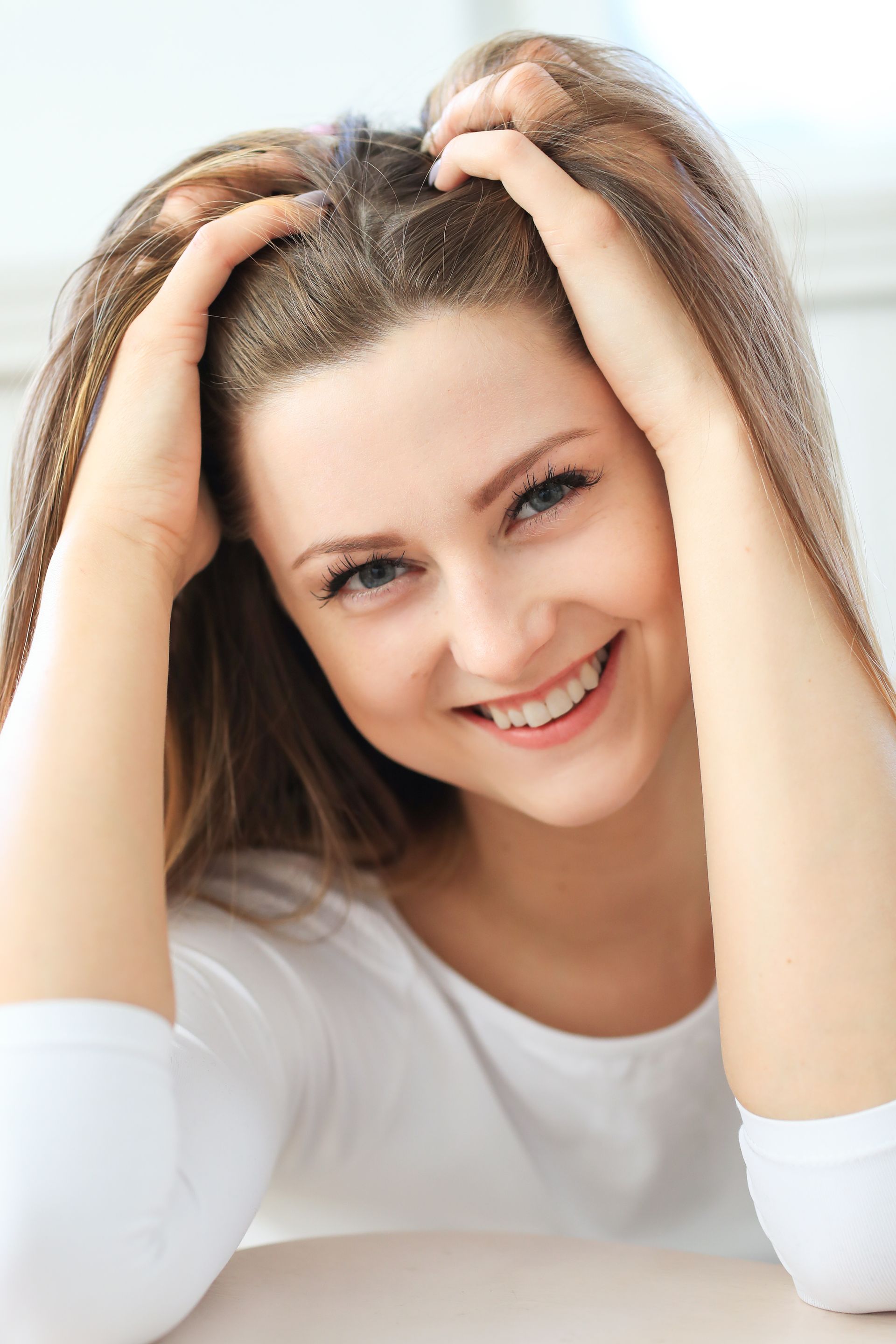 A woman is smiling and holding her hair in her hands.