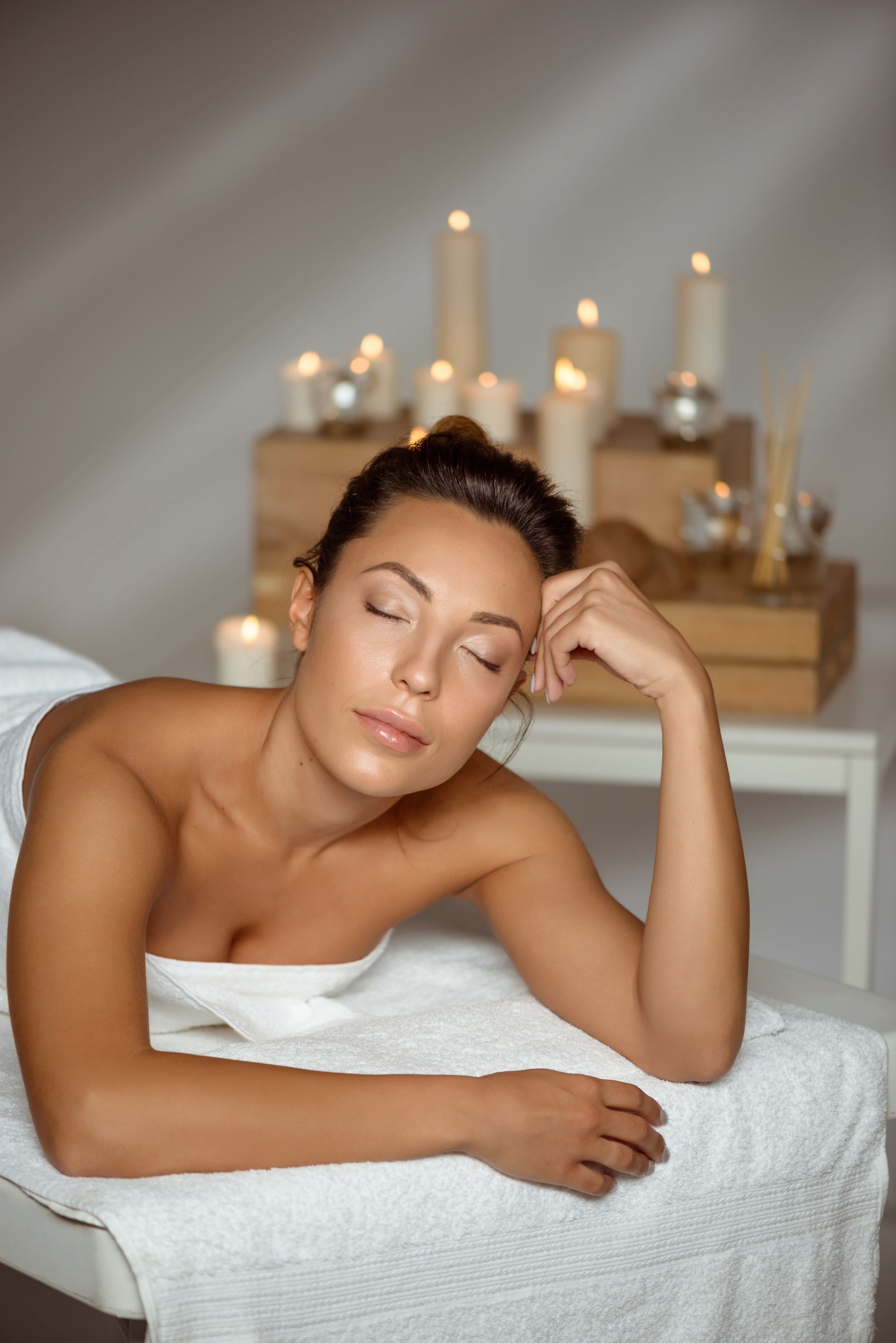 A woman is laying on a massage table with candles in the background.