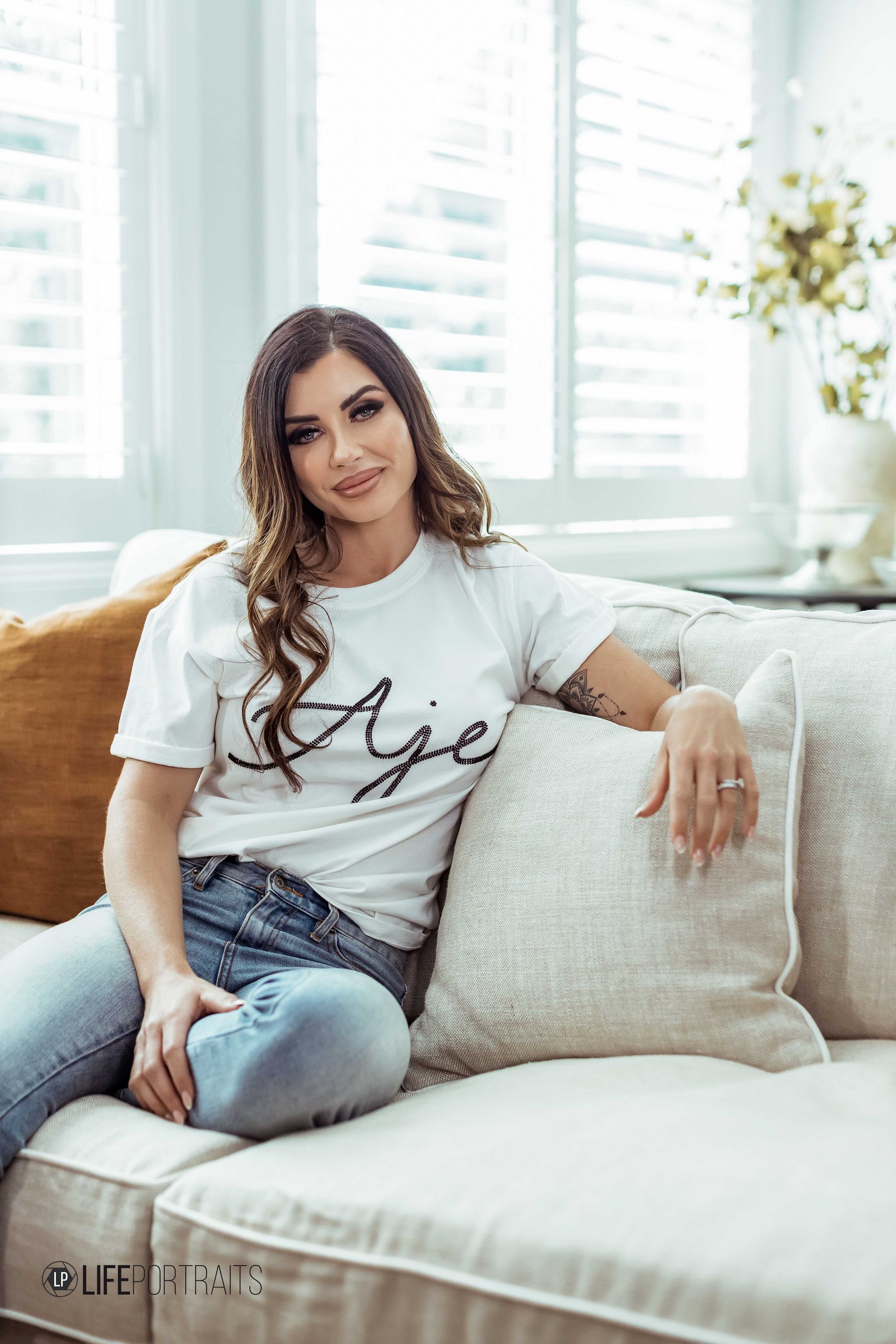 A woman is sitting on a couch wearing a white t-shirt and jeans.