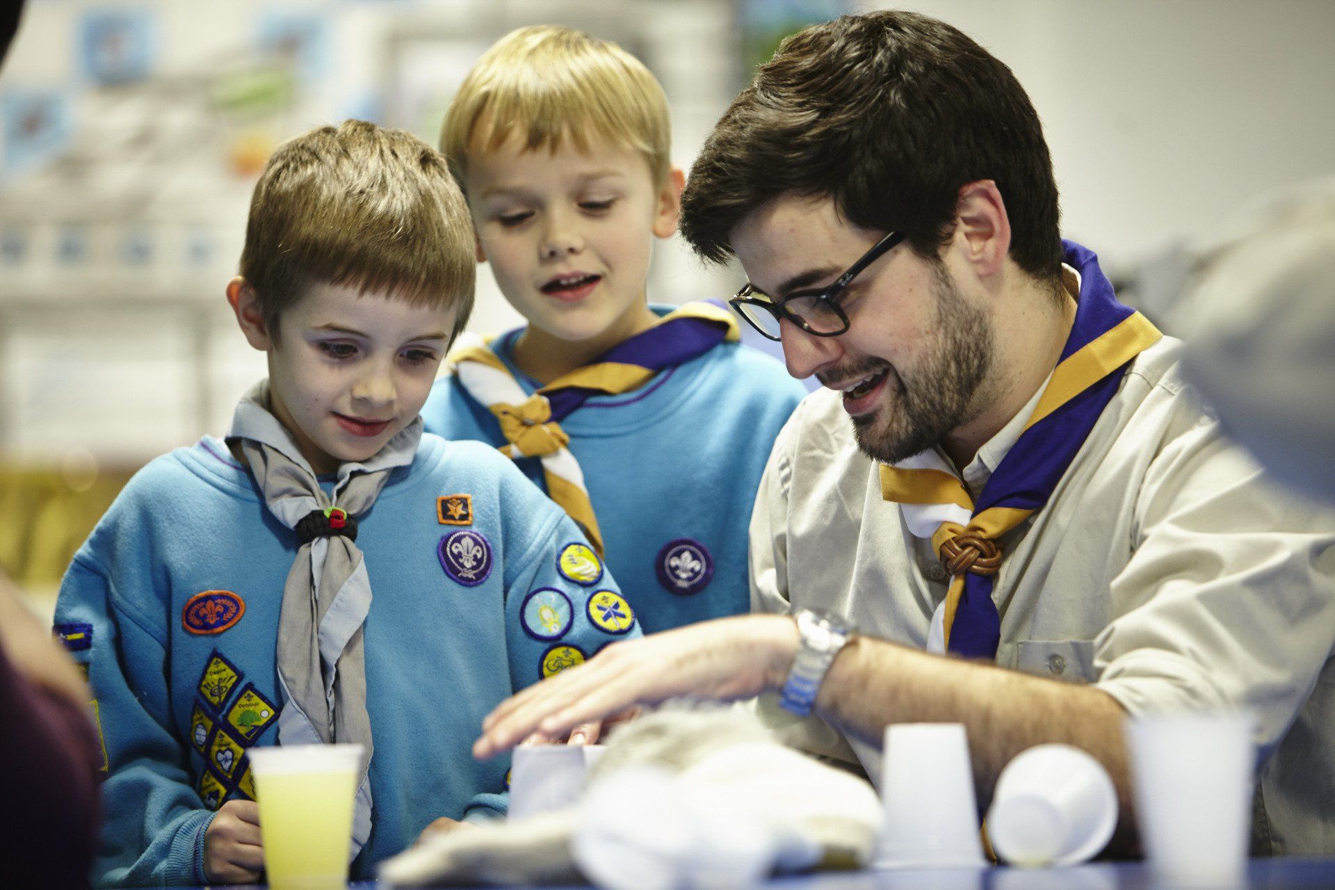 A man is talking to two boy scouts who are looking at something.