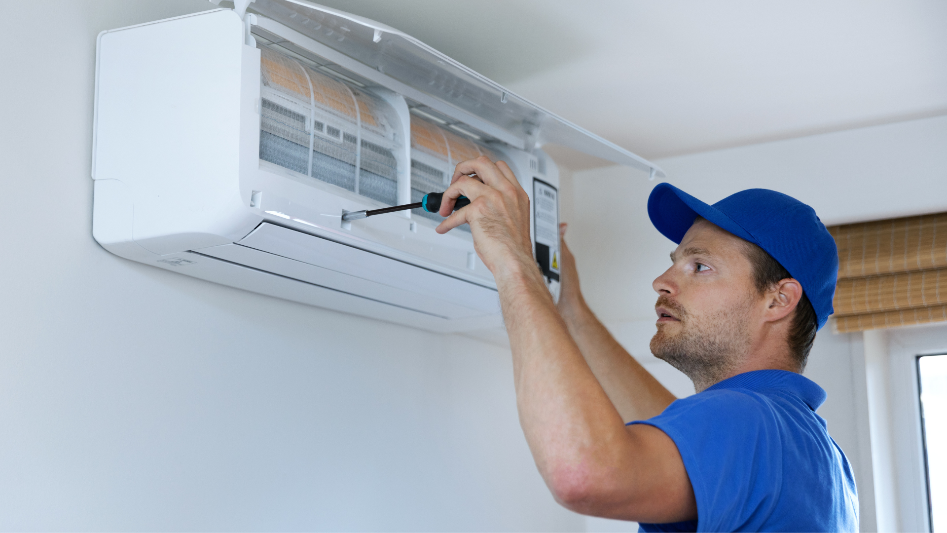 A man is fixing an air conditioner with a screwdriver.