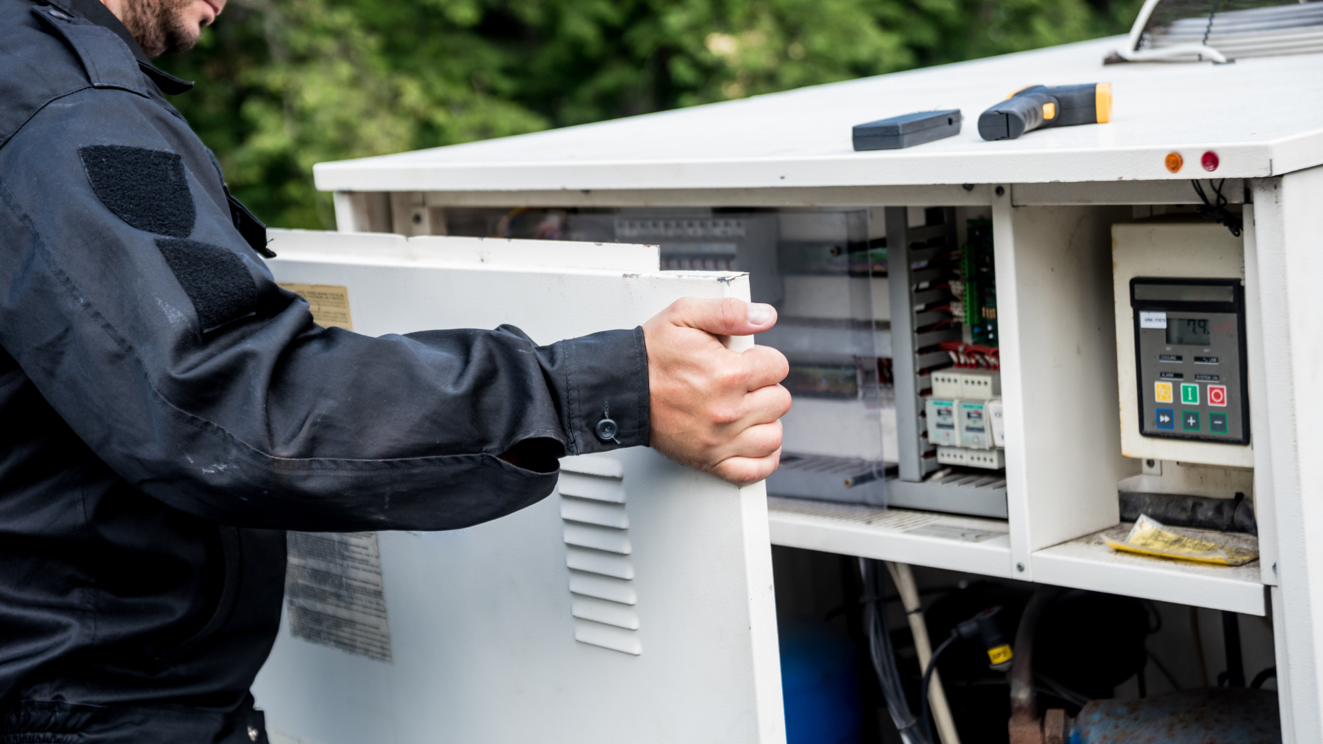 A man in a black uniform is opening a cabinet with a screwdriver.