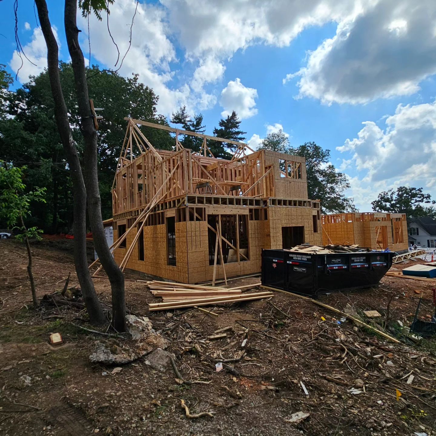 A house is being built on a hill with a dumpster in the foreground.