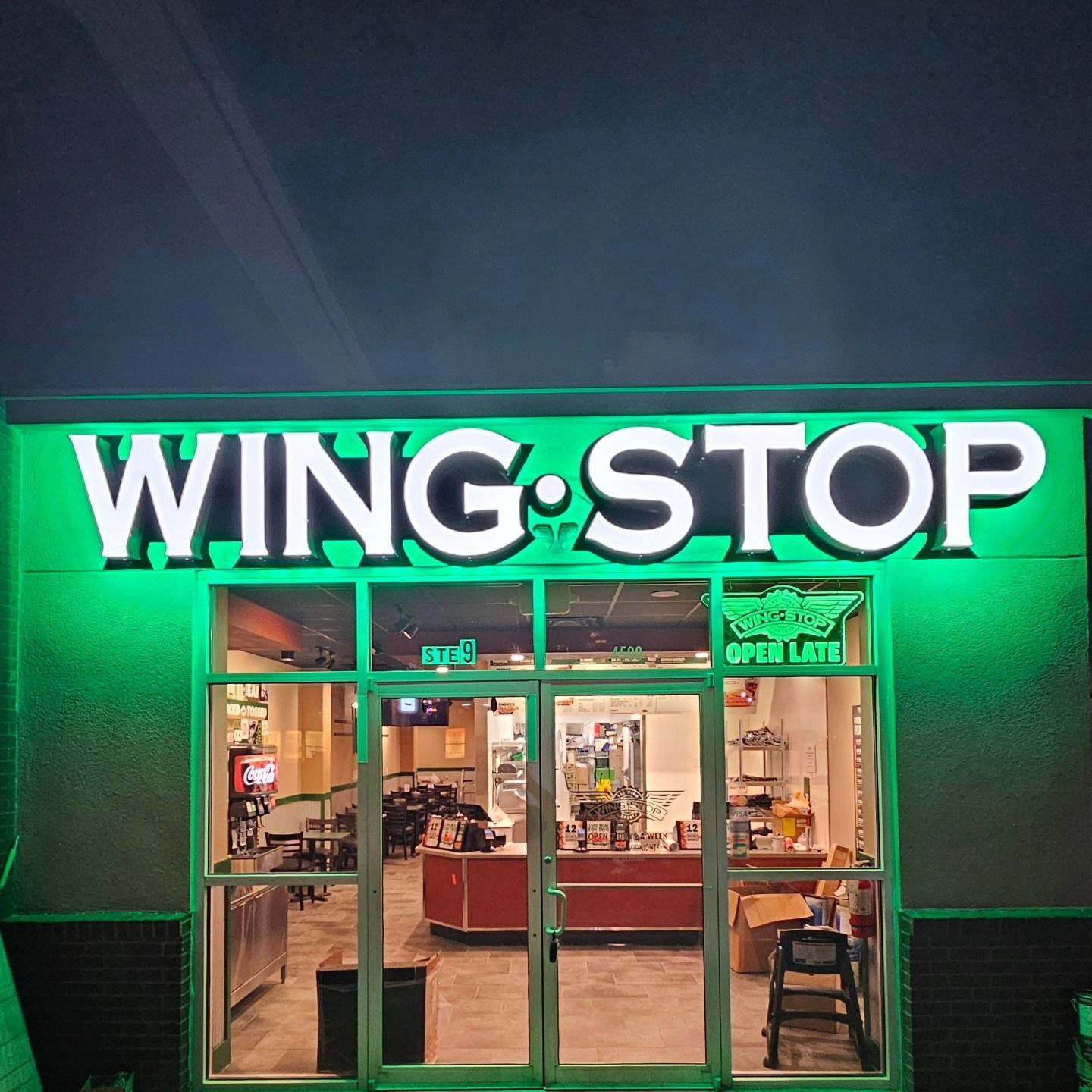 The front of a wing stop restaurant is lit up at night.