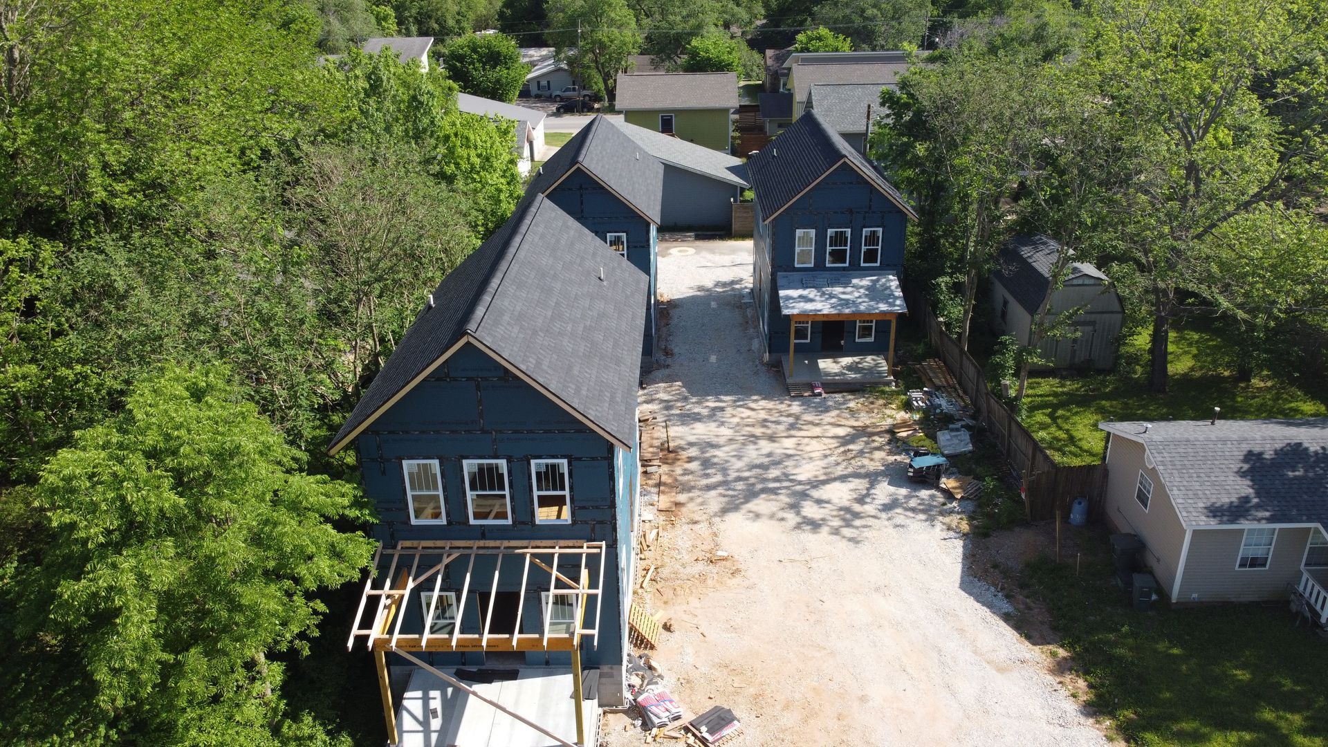 An aerial view of a house under construction in a residential area surrounded by trees.