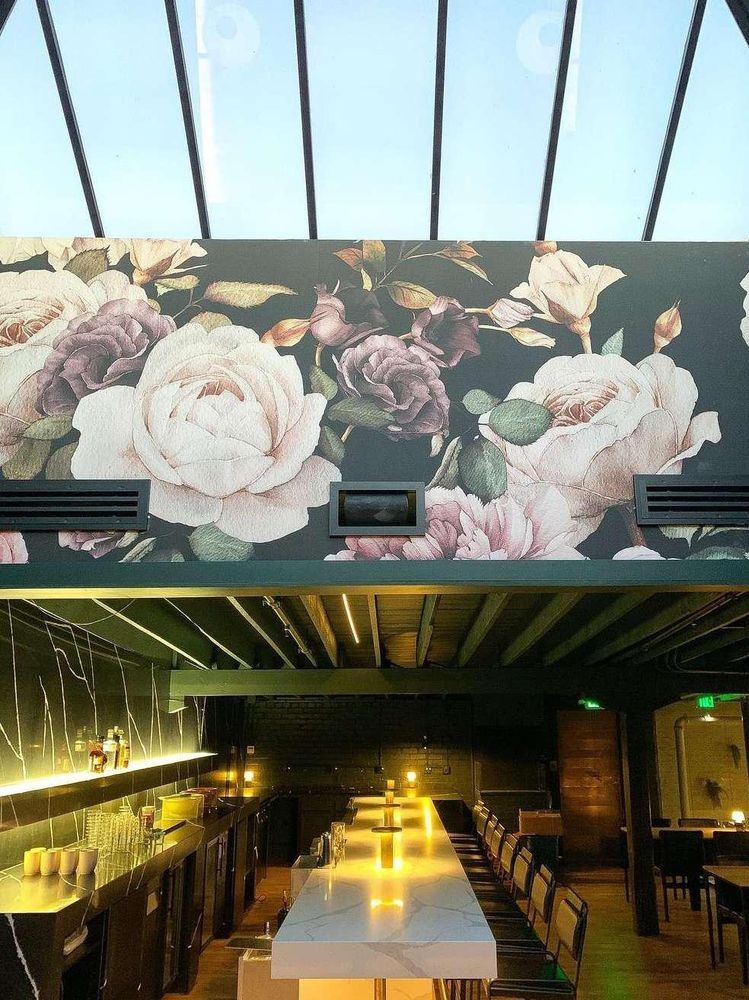 A restaurant with a long table and chairs and a floral wallpaper on the wall.
