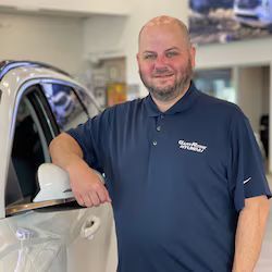 Josh Calkins is standing next to a white car in a showroom.