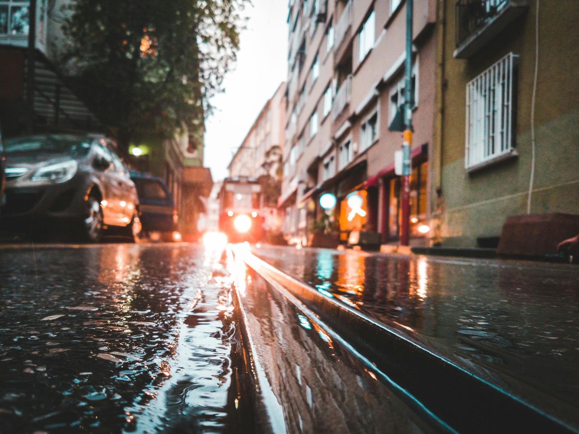A rainy city street with cars parked on the side of it